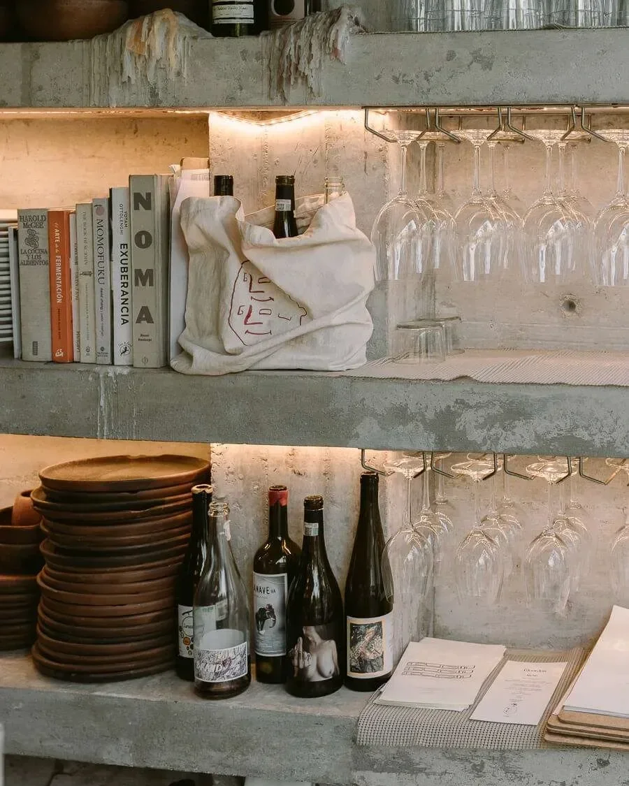 Shelves with books, bottles, wine glasses, plates, and menus in a restaurant or cafe setting.