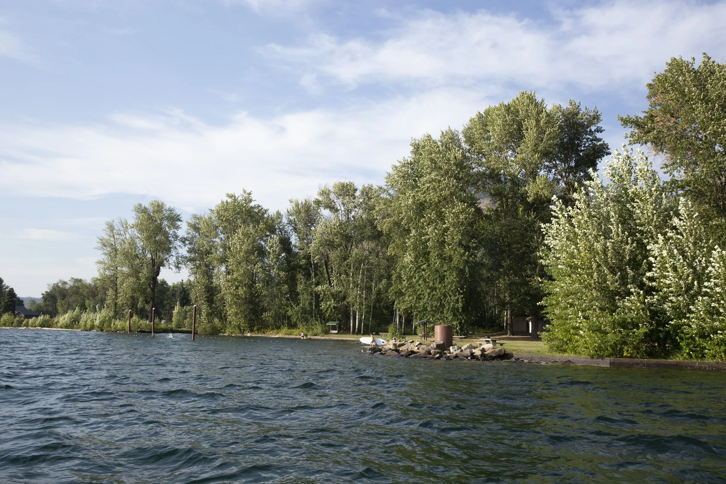 A peaceful stretch of shoreline at Trestle Creek Recreation Area, where calm water, mature trees, and a quiet beach create an inviting place to launch, explore, or simply enjoy Lake Pend Oreille.