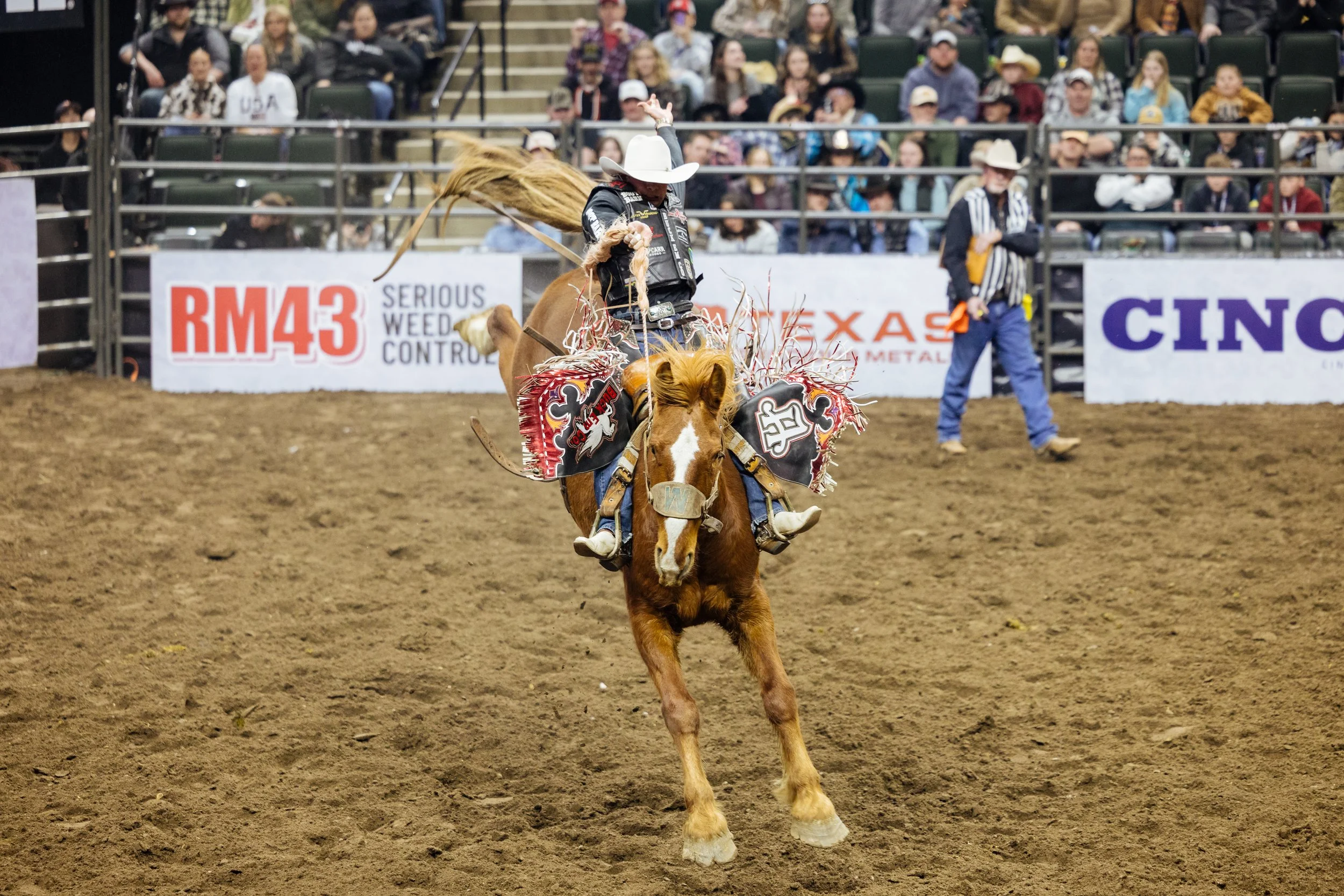 A cowboy riding a bucking bull during a rodeo event, with an audience watching from the stands.