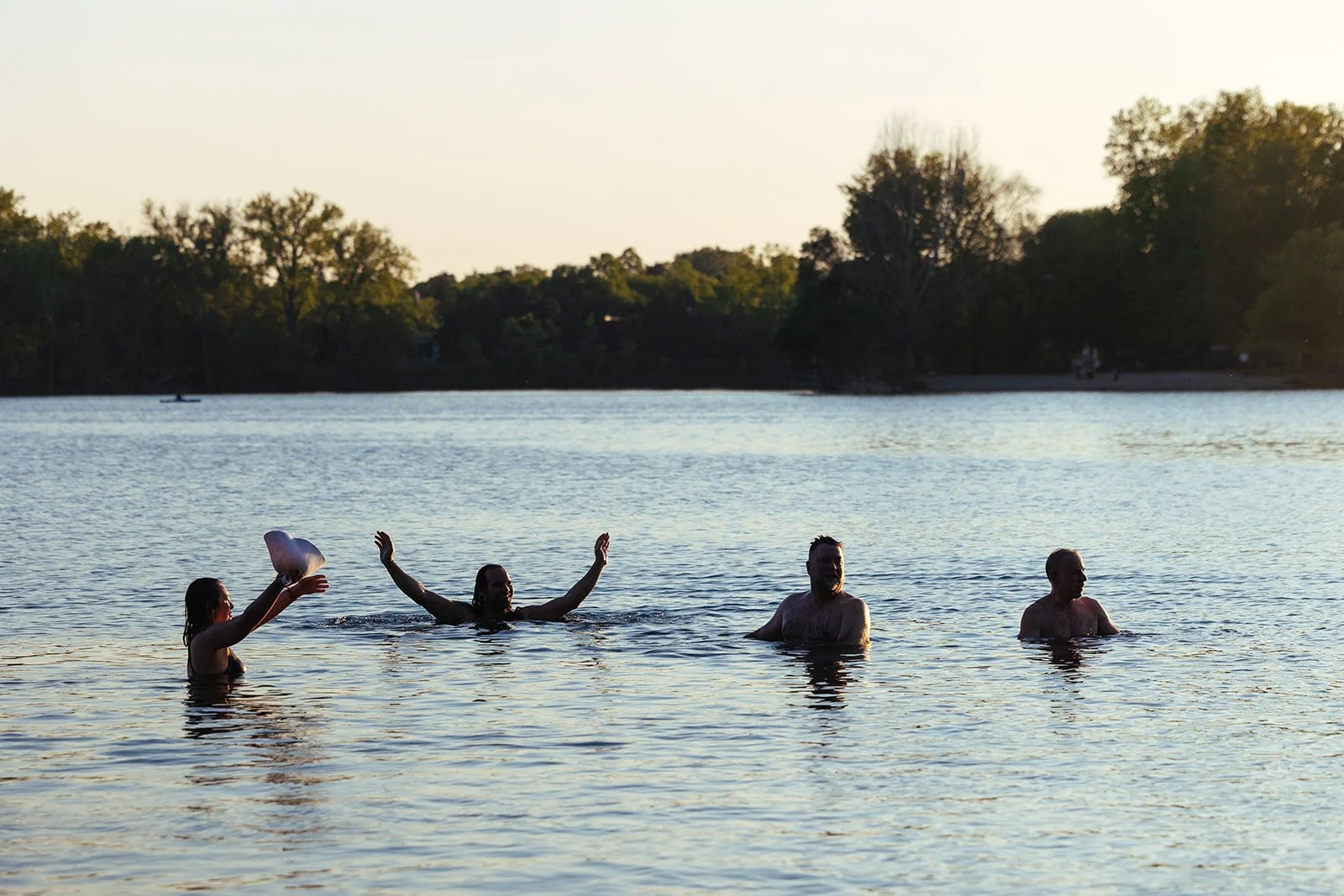 Group of four adults swimming and playing in a lake during sunset.