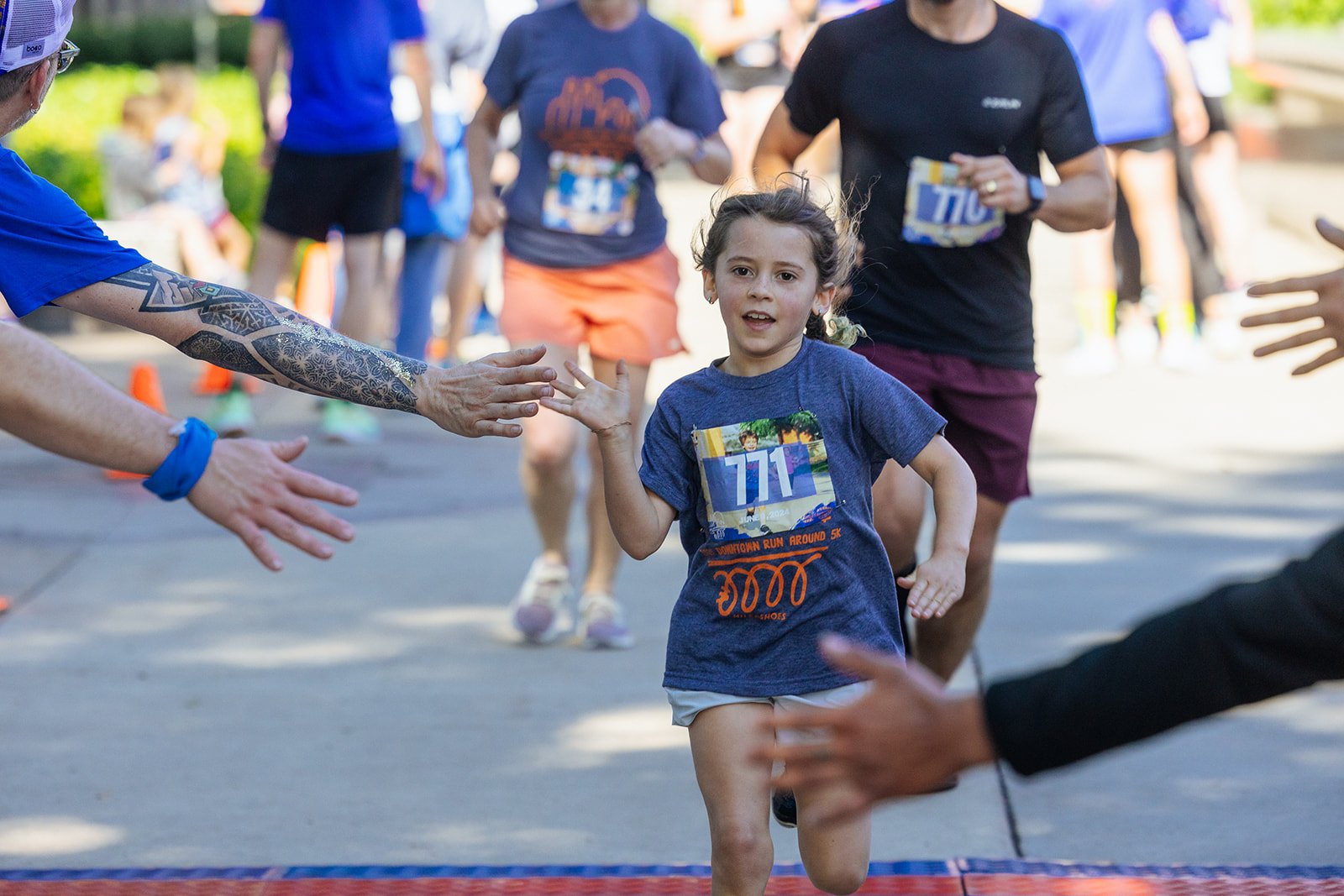 A young girl running a race and high-fiving volunteers at the finish line during a community running event.