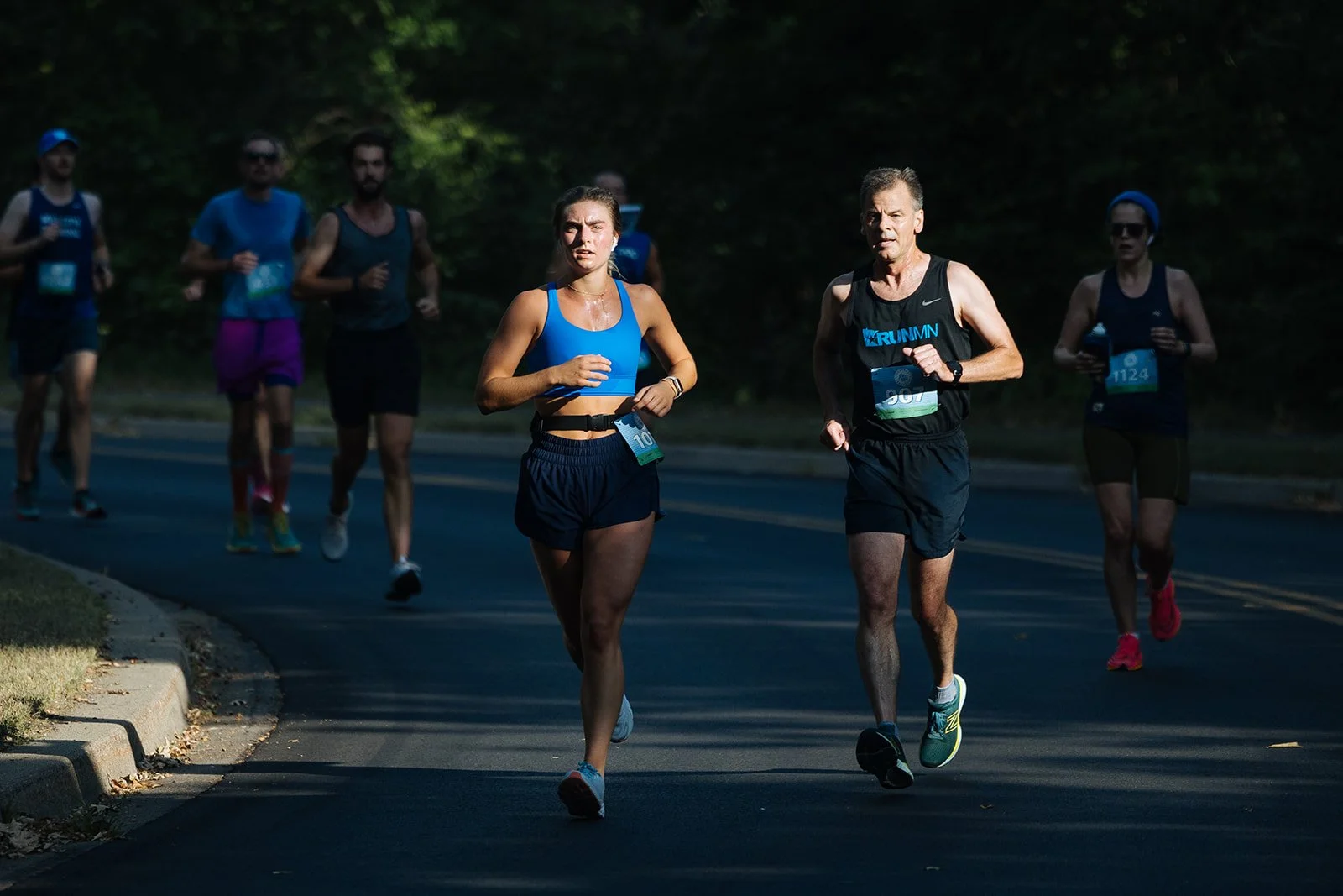 Group of people running on a paved road during a race, surrounded by trees and greenery.