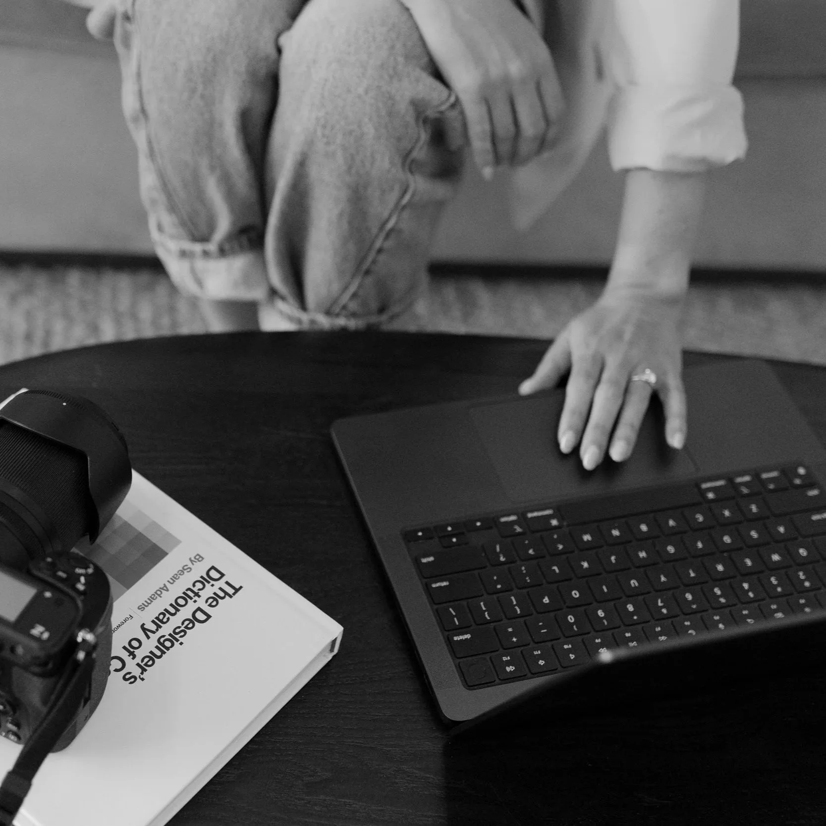 A person sitting at a desk with a keyboard, a tablet, a monitor, a book titled 'The Design of Everyday Things,' and a pair of headphones on the desk.