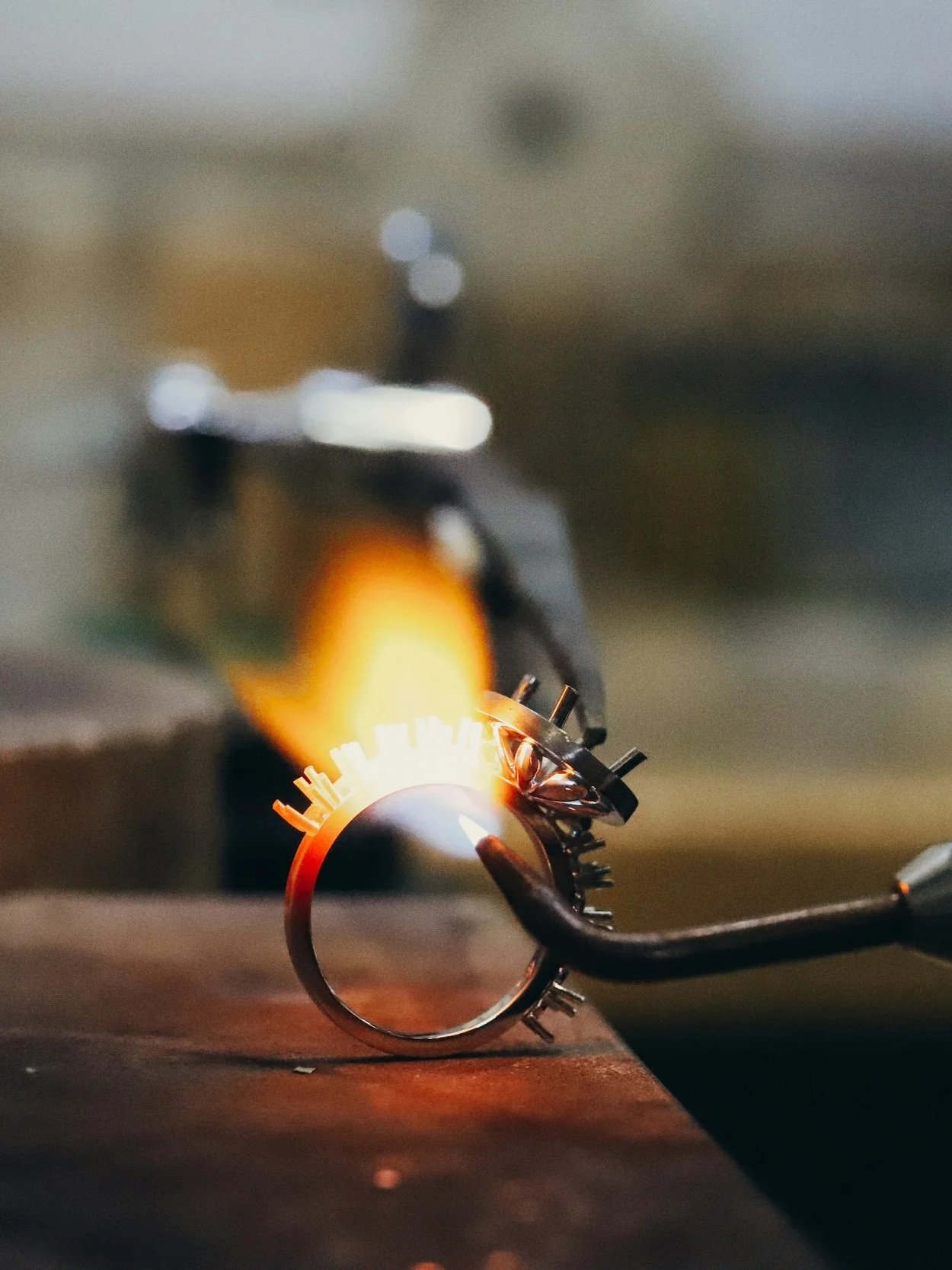Imagem de processo de soldagem, com uma chama emanada de uma peça metálica sendo trabalhada, superfície de trabalho escura e foco no brilho da solda.