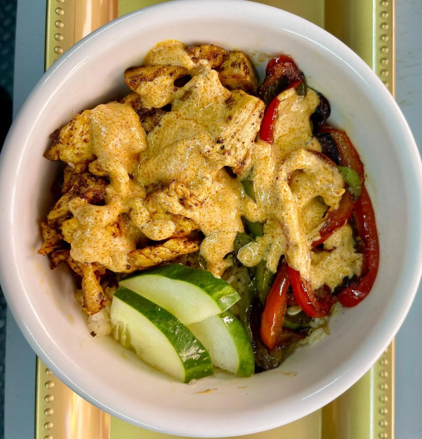 A bowl of chicken fajitas with grilled chicken, sautéed red and green bell peppers, and onions topped with a creamy sauce, served with lime wedges.