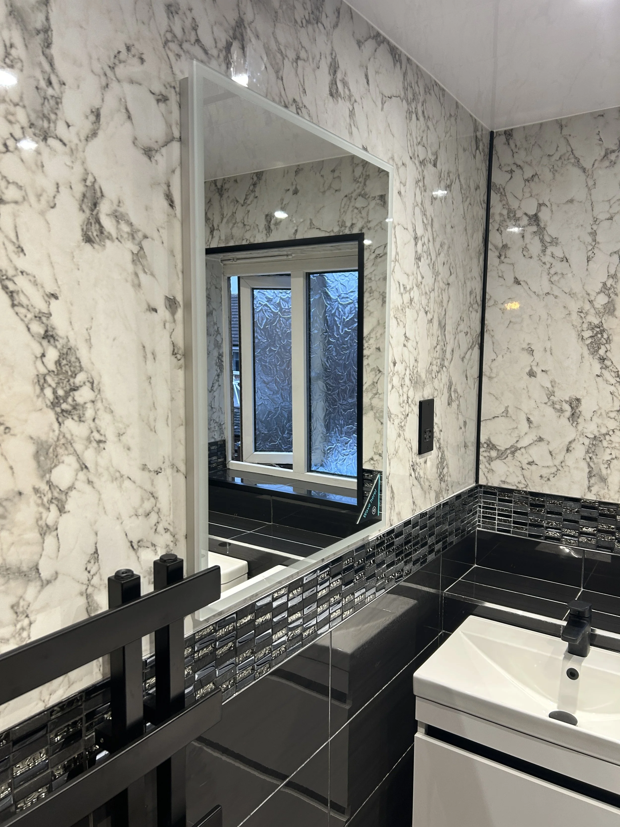 A modern bathroom with marble-patterned walls, a black and silver tiled backsplash, a black towel rack, and a white sink with a black faucet.