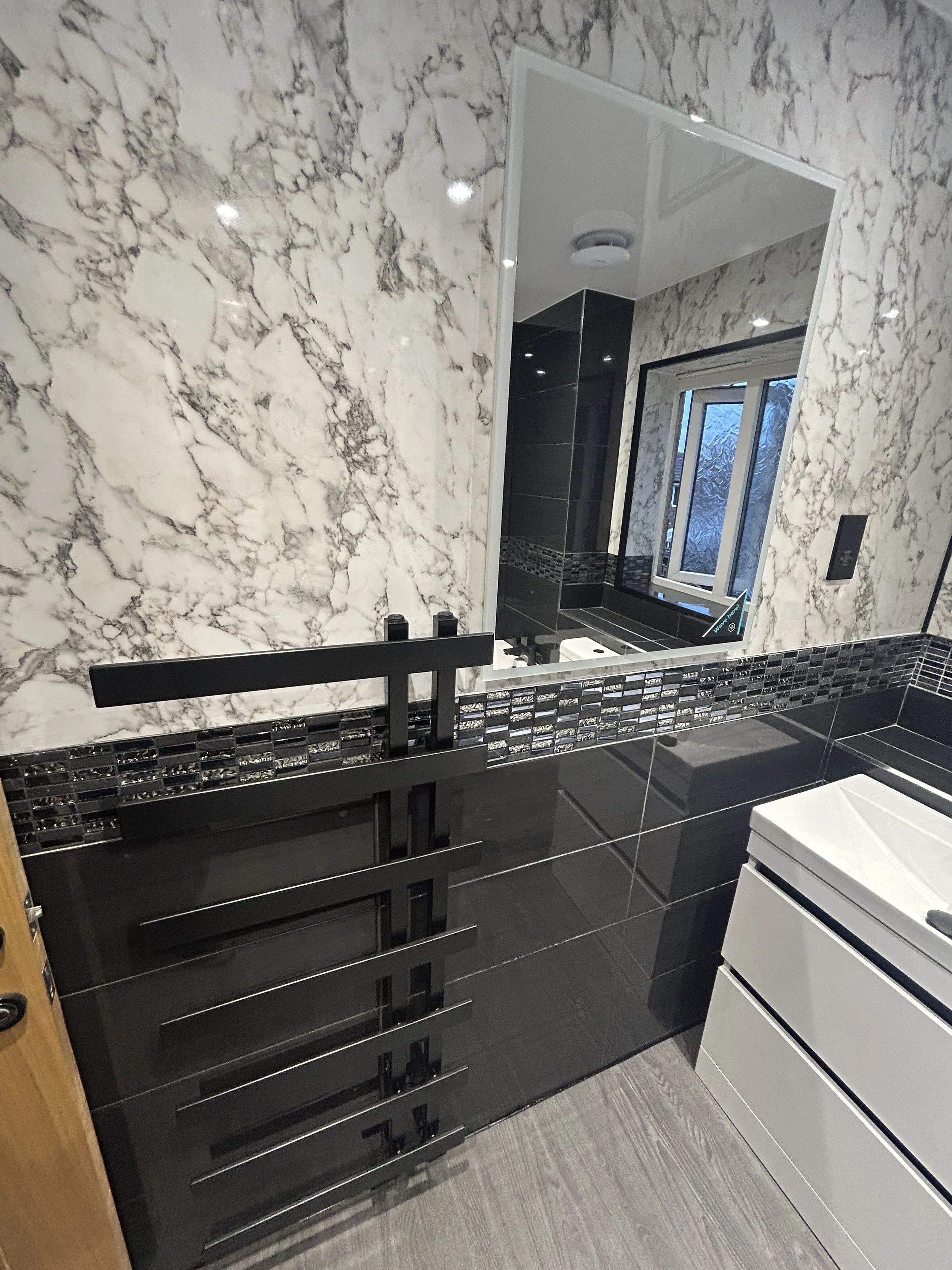 Bathroom with marble wall, black vanity with open shelves, large mirror, and window with textured glass.