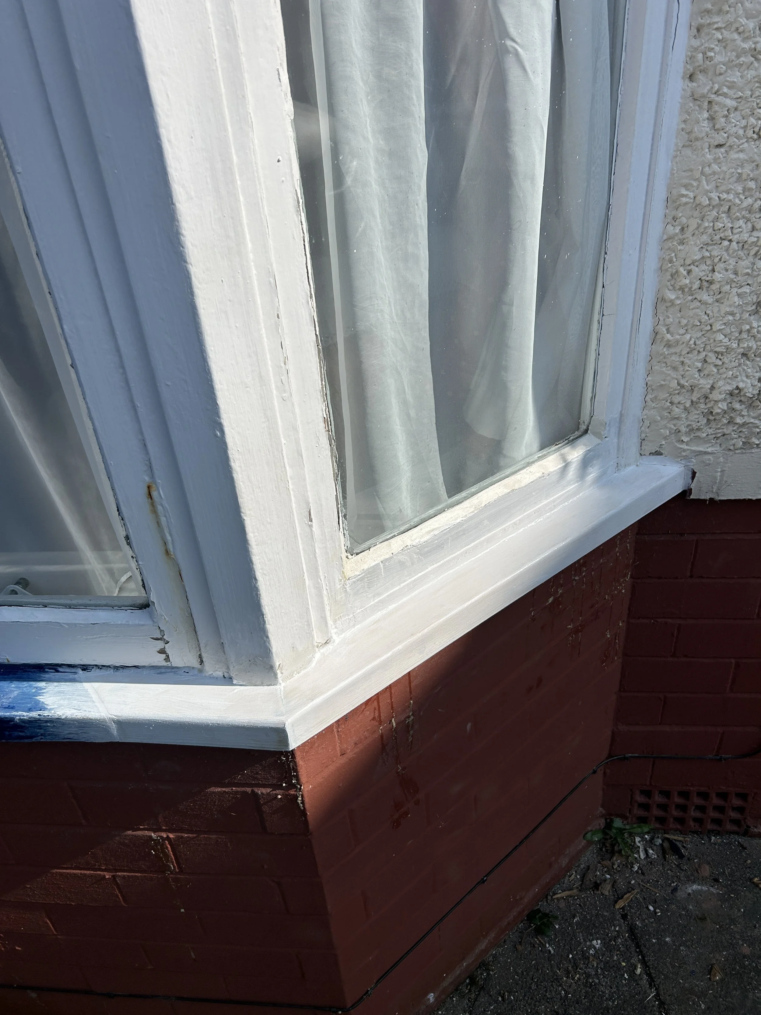 Close-up of a white window frame with curtain inside on a red brick wall exterior.