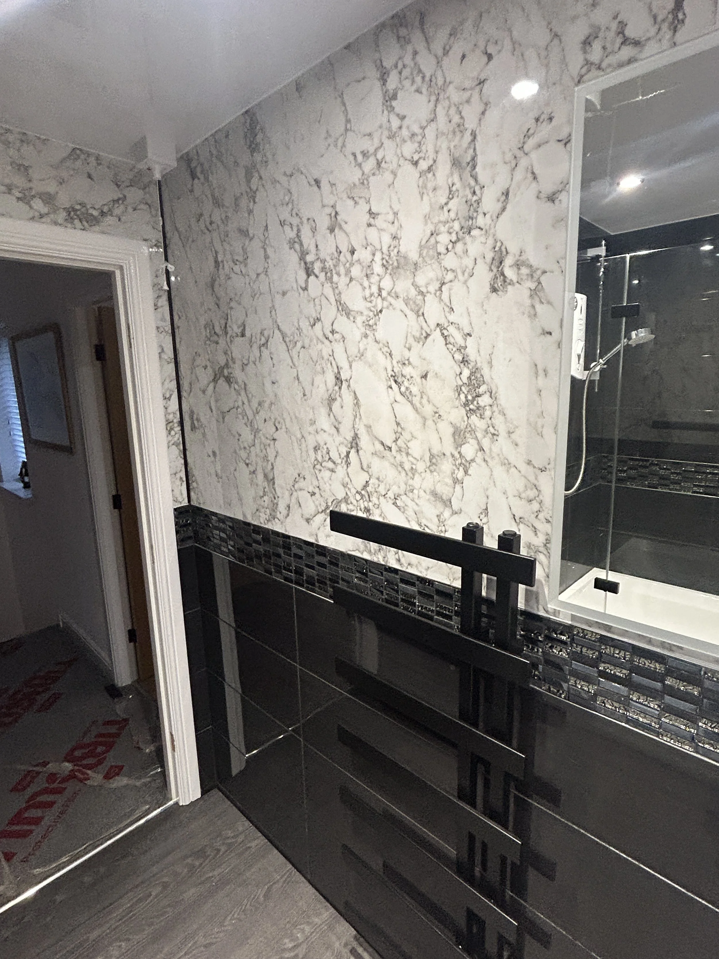 Bathroom with marble wall tiles, black vanity, and a shower area with black tiles and a glass door.