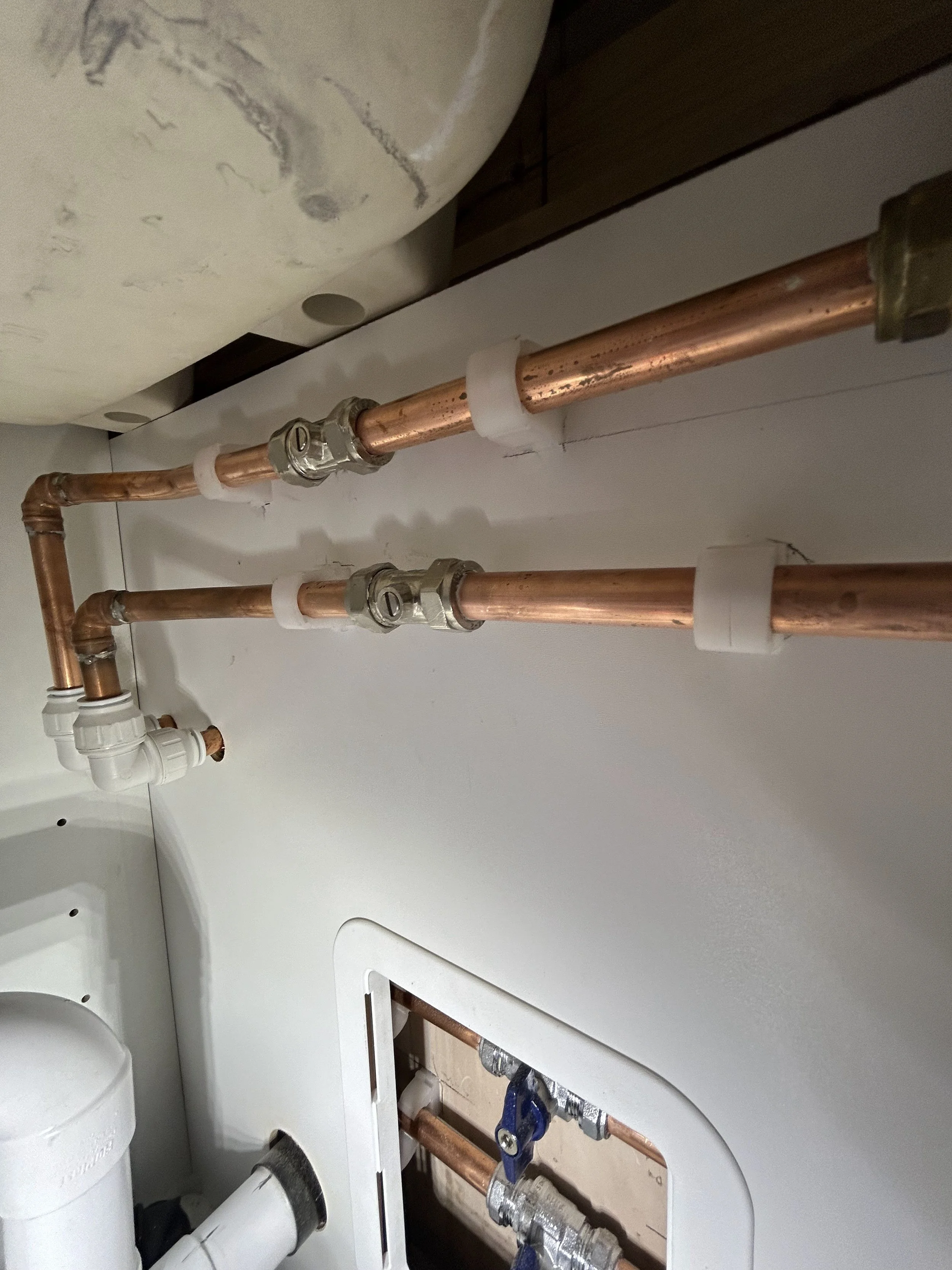 Copper plumbing pipes installed behind a drywall panel with white pipe fittings and valves.