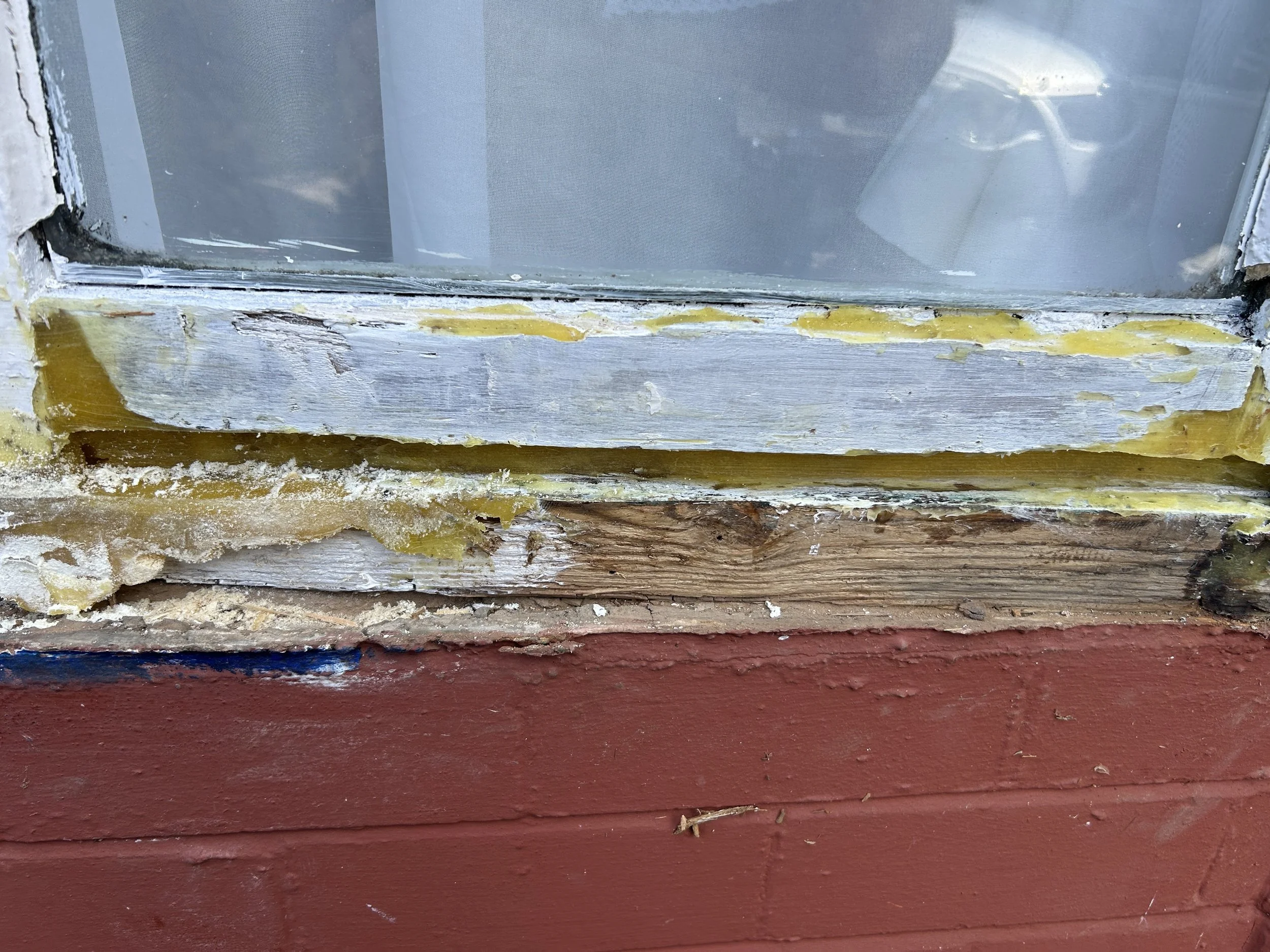 Close-up of a window frame with peeling paint and weathered wood, overlooking a cloudy sky.