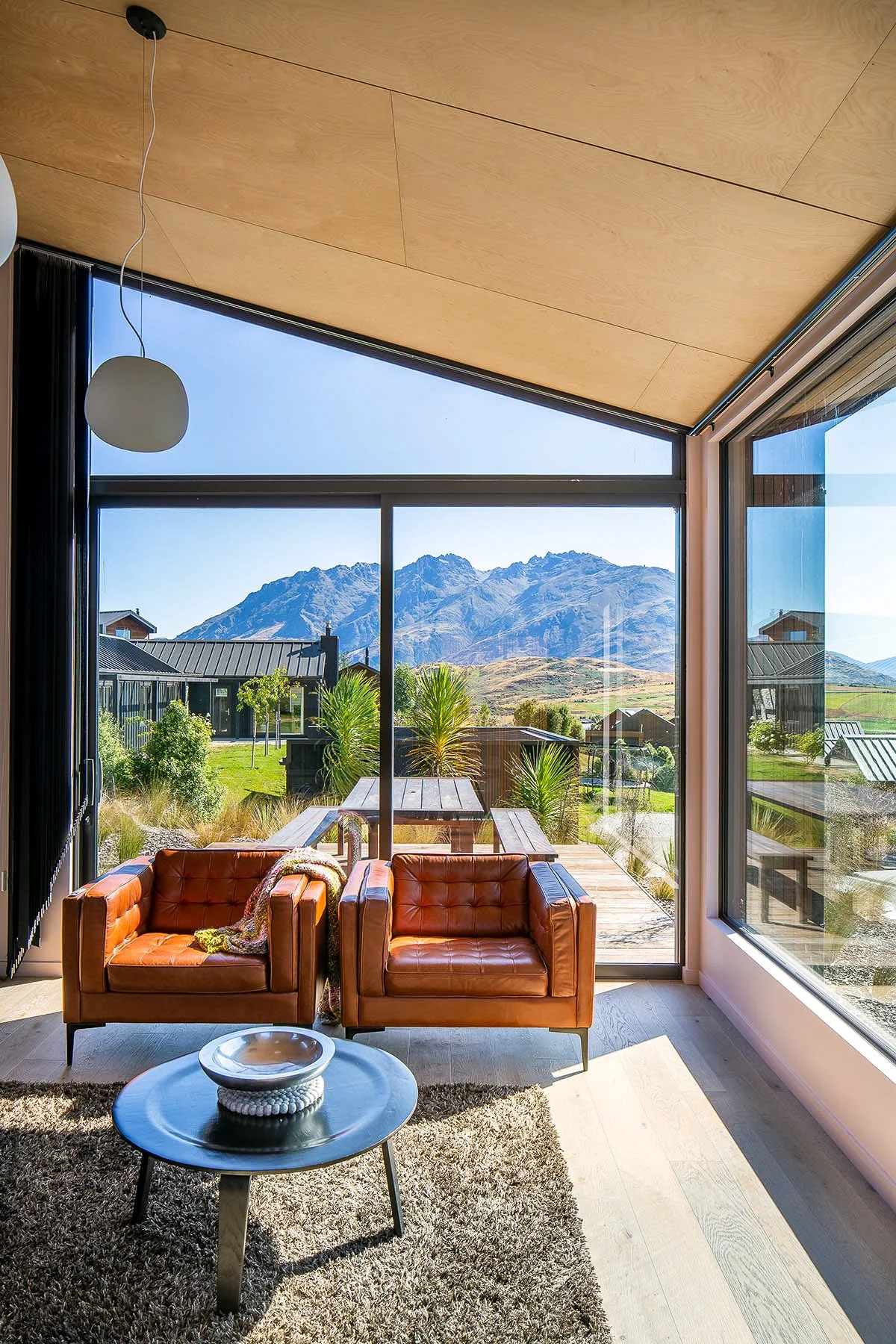 Modern living room with leather armchairs, round coffee table, and mountain views through floor-to-ceiling windows