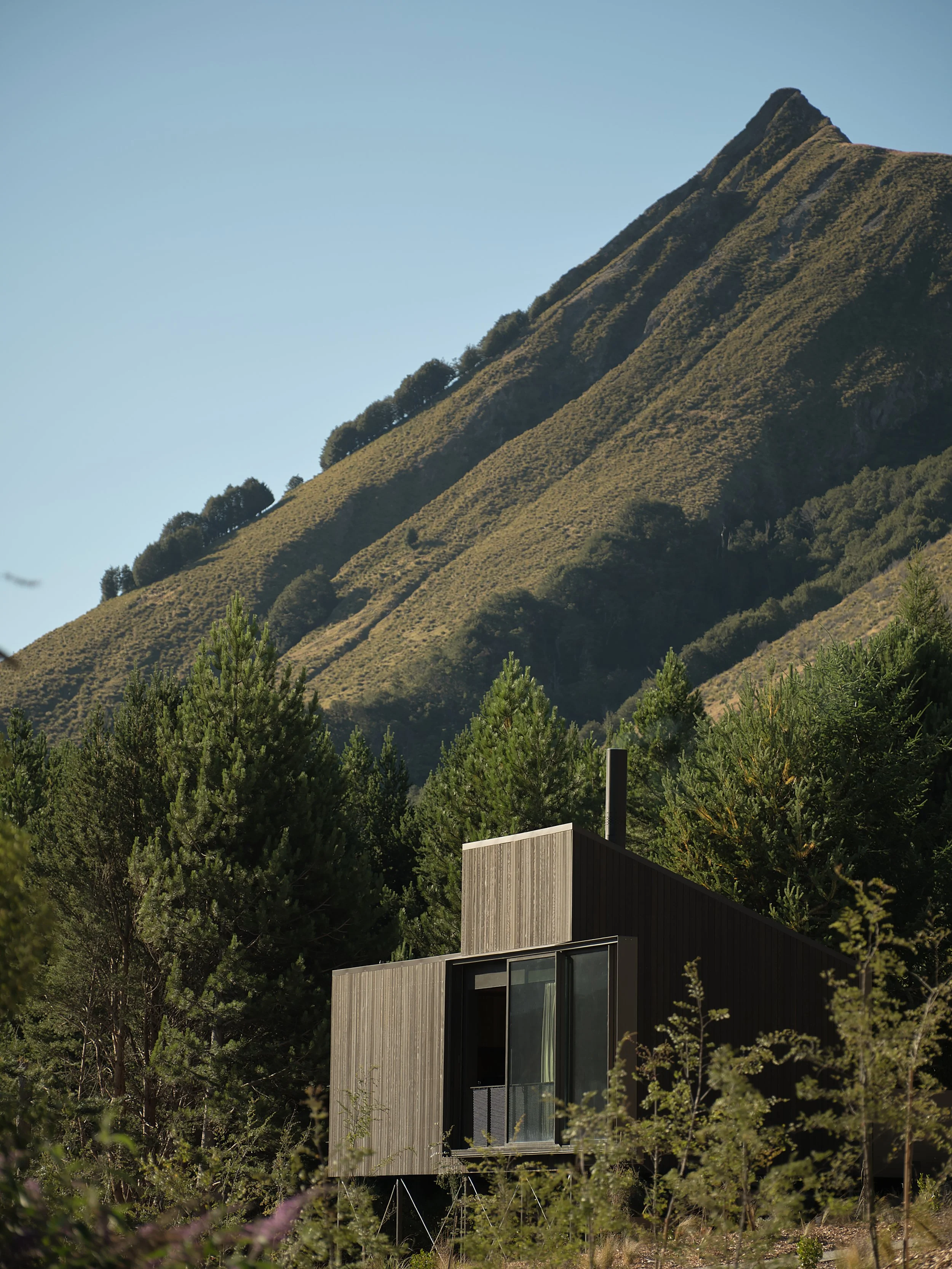 Modern woodland cabin beneath a rugged, forested mountain peak