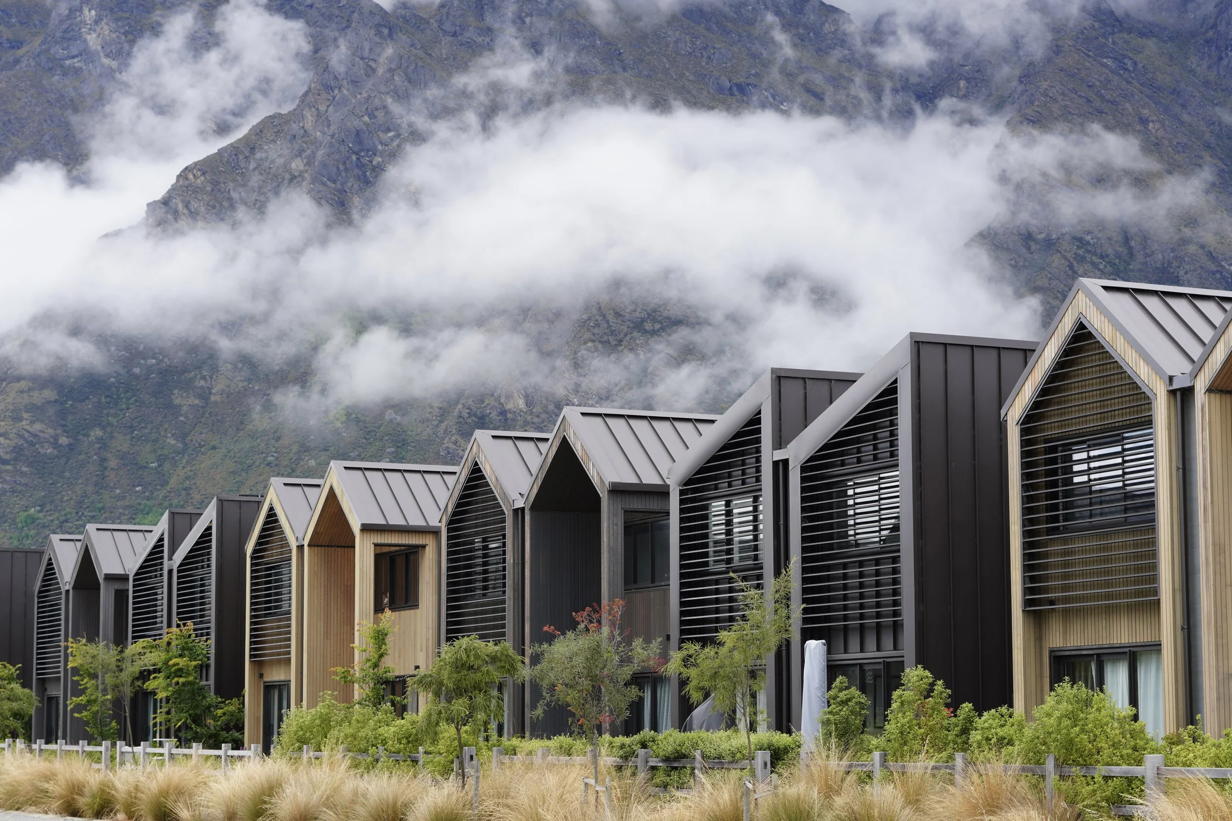 Modern alpine homes with steep gabled roofs beneath mist-covered mountains