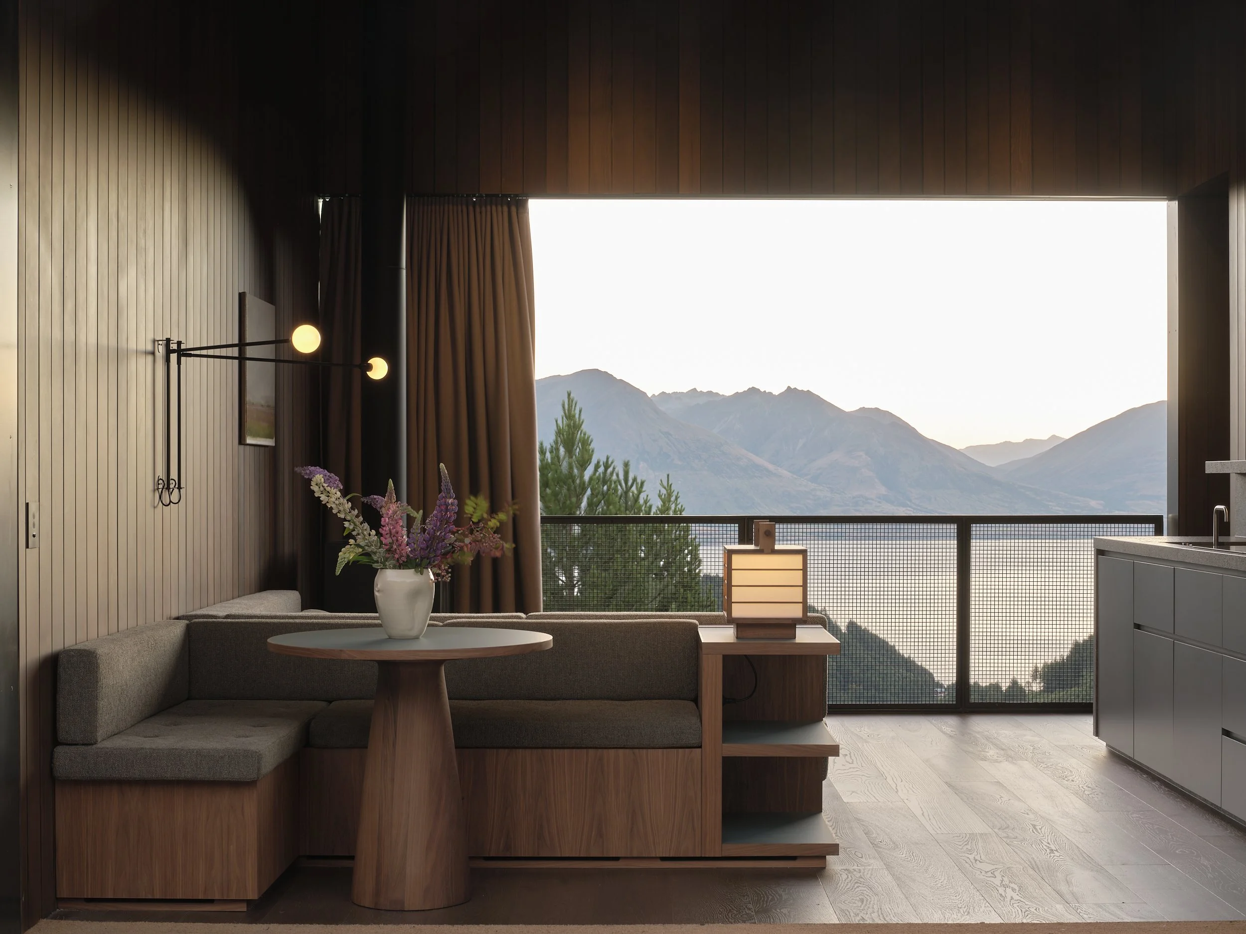 Modern living room with a sectional sofa, round table, flowers, and mountain views through a large window