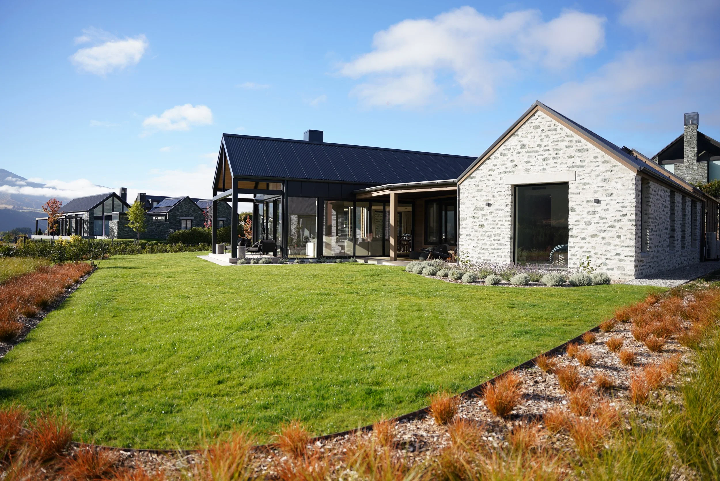 Modern stone-and-black-roof homes with landscaped lawns and mountain views under a blue sky