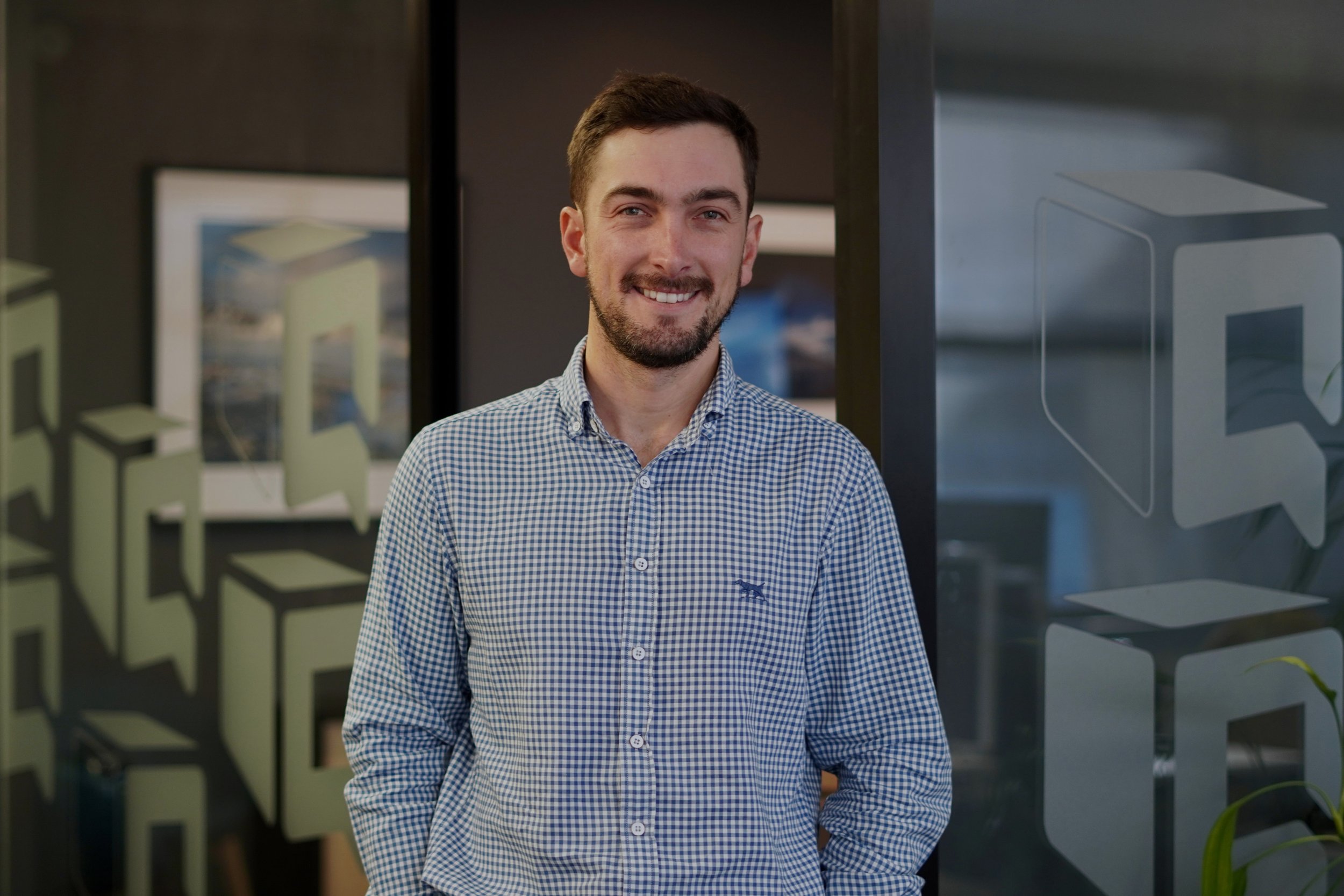 Smiling man in a blue-and-white checkered shirt standing in a modern office