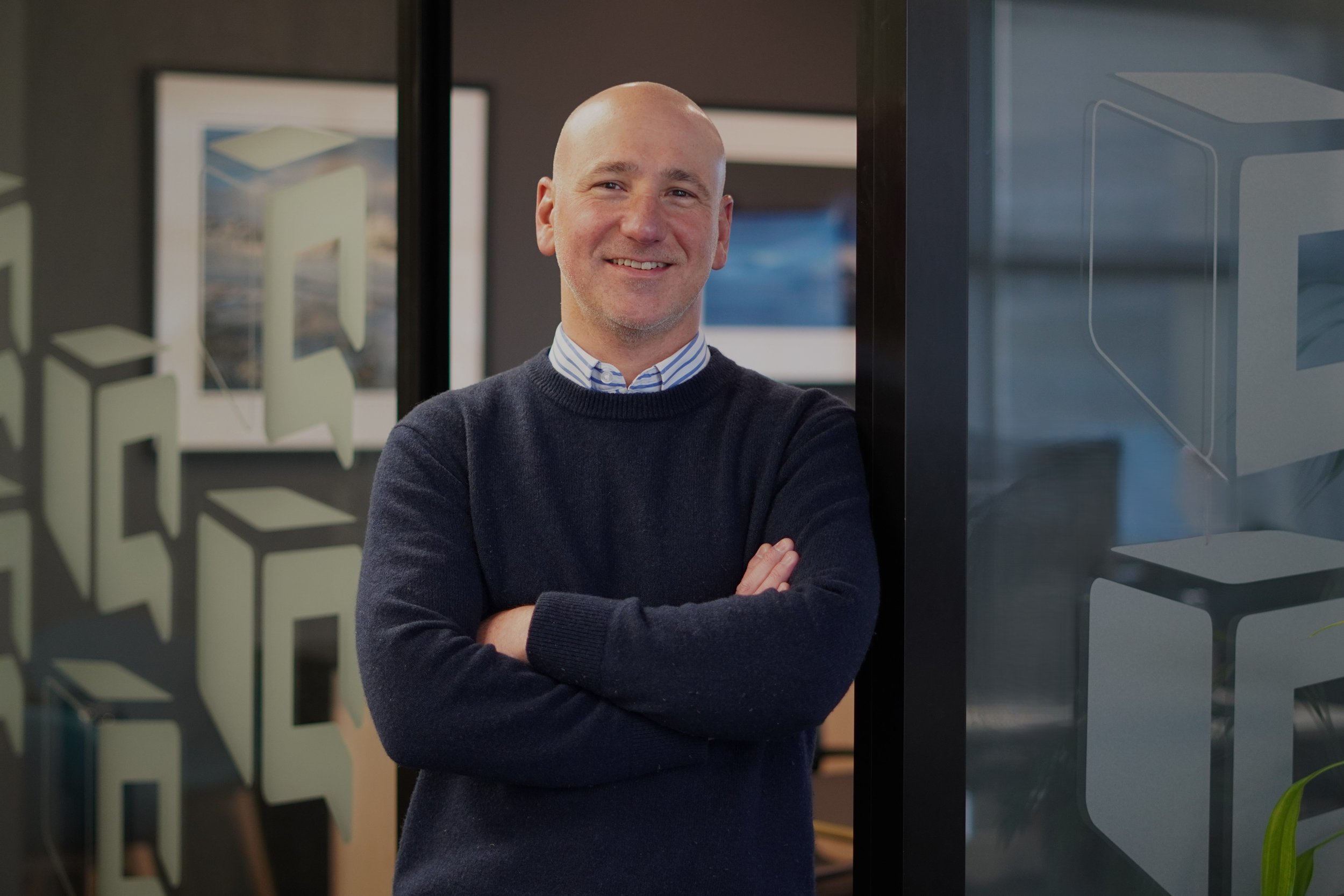 Smiling bald man with folded arms standing in a modern office