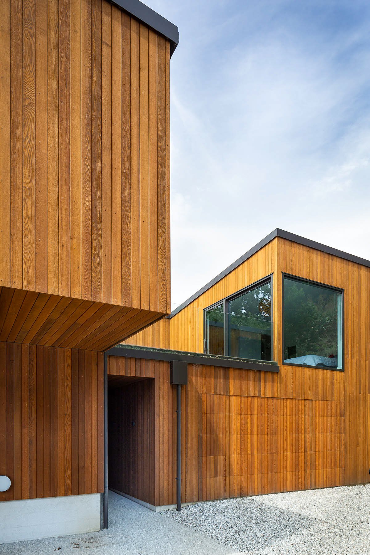 Modern wood-clad house with black trim, geometric rooflines, large windows, and gravel landscaping