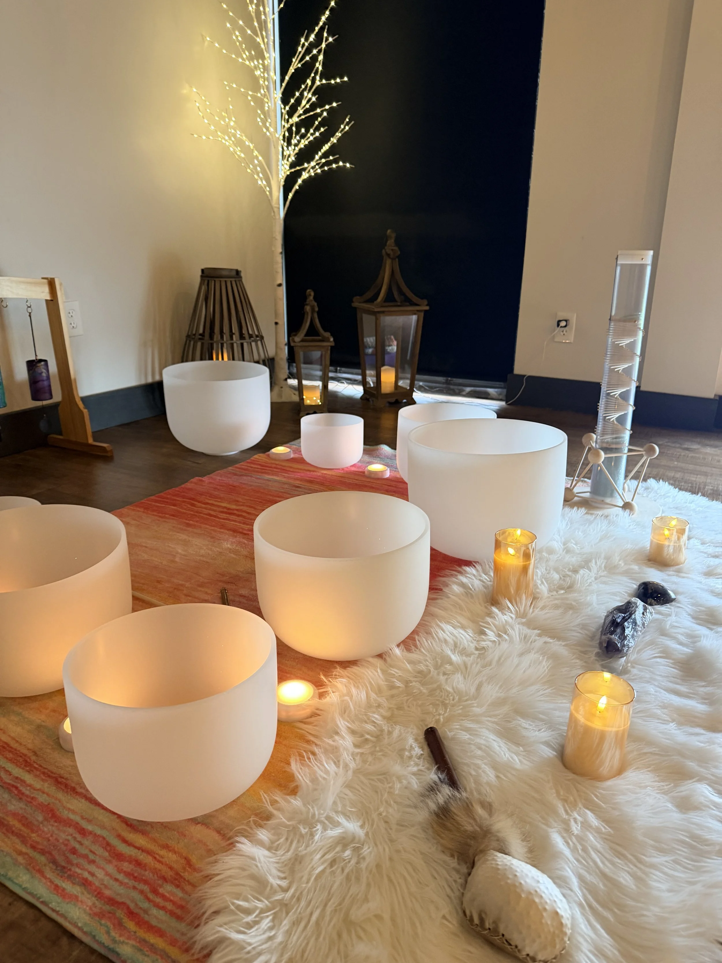 Cozy meditation or relaxation space with lit candles, soft furry rug, wooden lanterns, and decorative objects, in a room with a dark blue accent wall. yoga sound healing sound bath event for private parties crystal singing bowls
