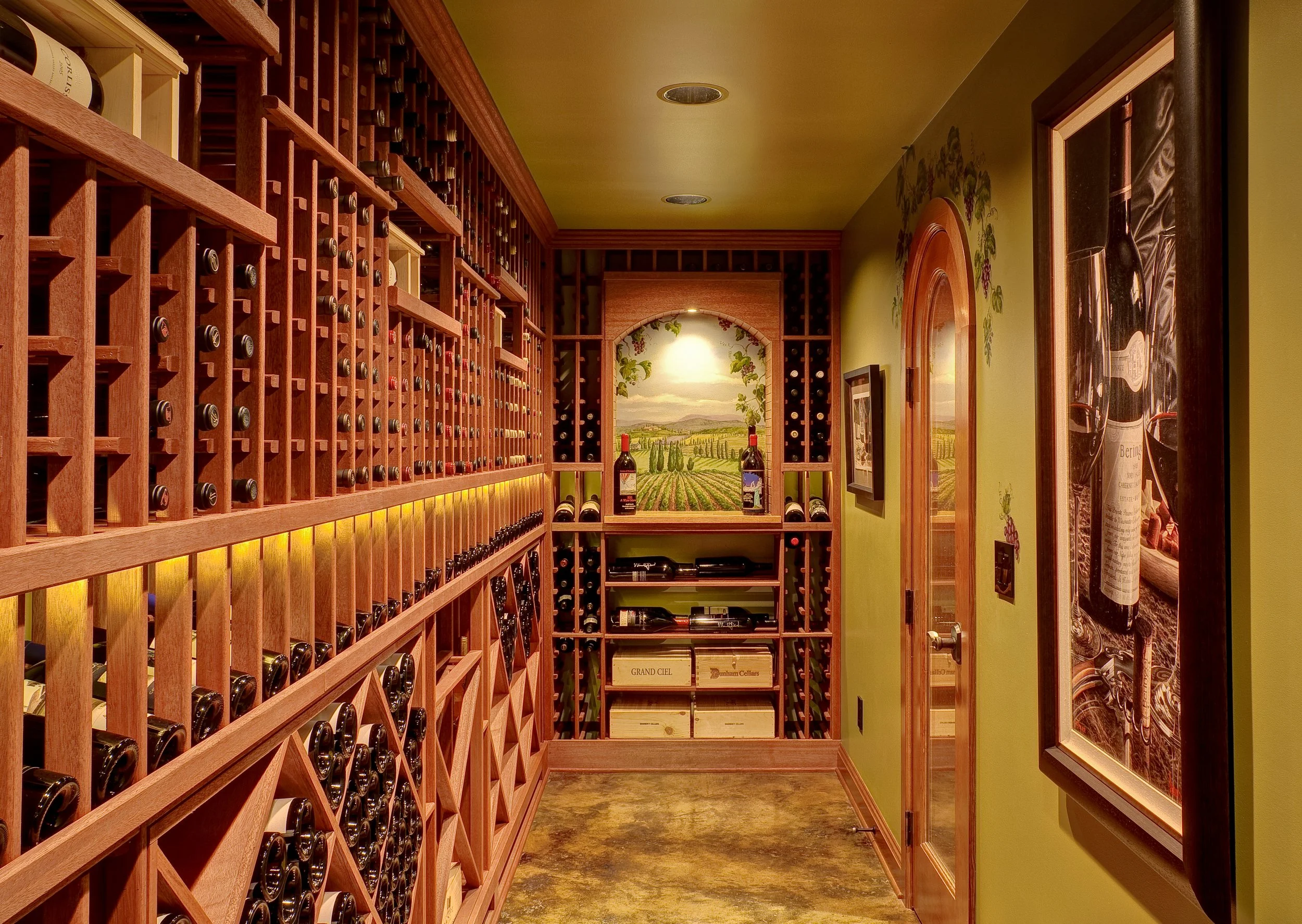 warm rustic basement wine room remodel with arched glass doorway, mosaic wall accents, stamped concrete flooring, and layered ambient lighting