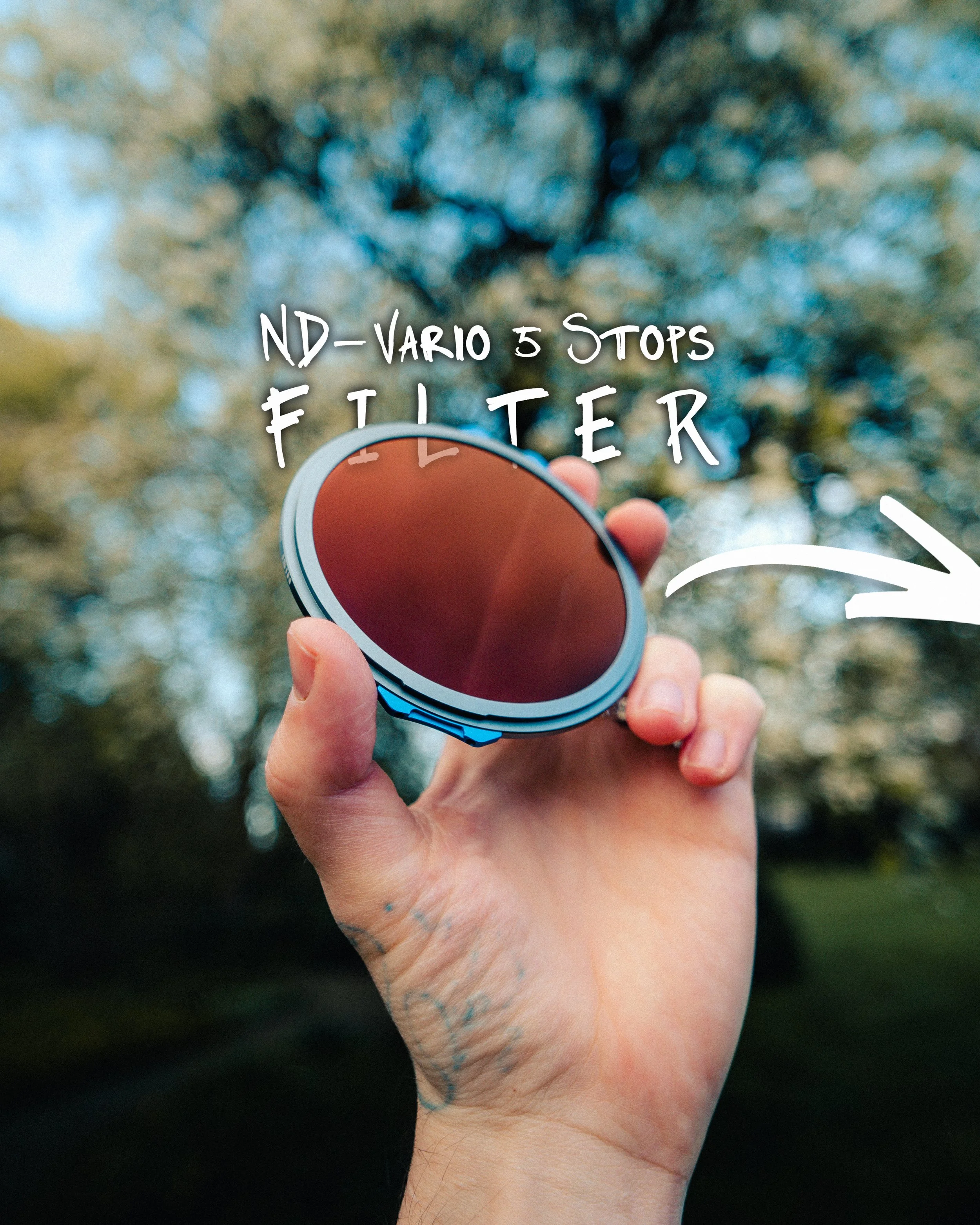 Hand hält einen runden Filter mit mattschwarzer Oberfläche vor einem Baum im Freien, im Hintergrund blauer Himmel und Blätter. Text auf Bild: 'ND-VARIO 5 STOPS FILTER'.