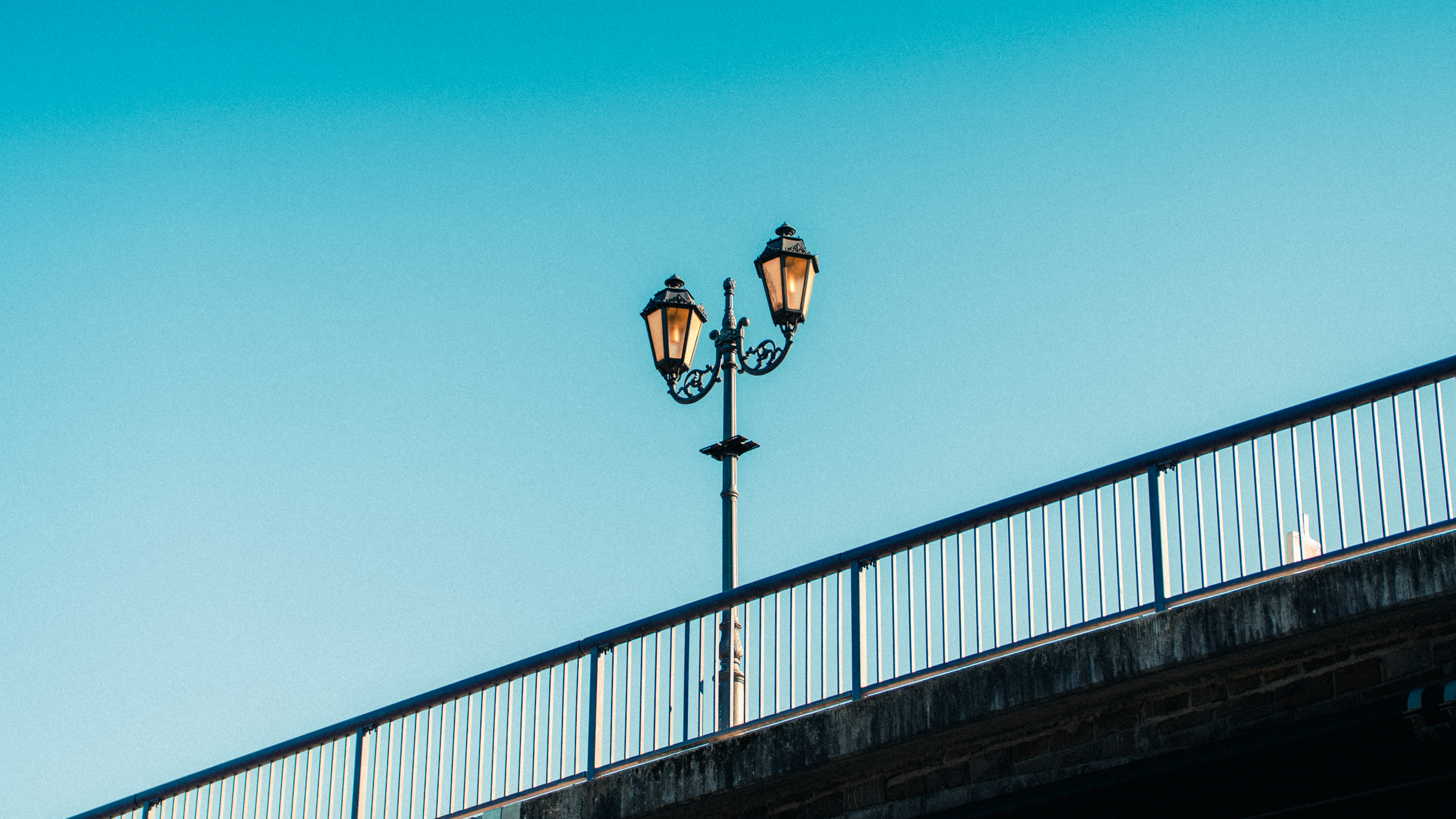Straßenlaterne auf einer Brücke gegen blauen Himmel.