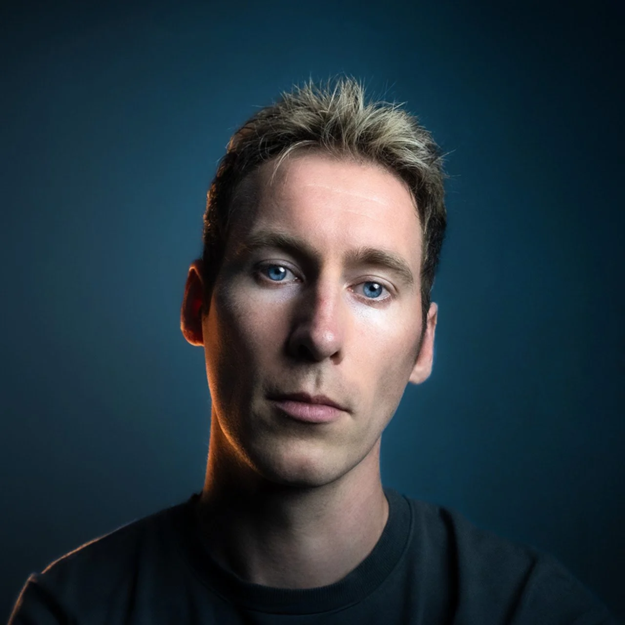 Porträt eines jungen Mannes (Kevin Piatek) mit blauen Augen vor dunklem Hintergrund.