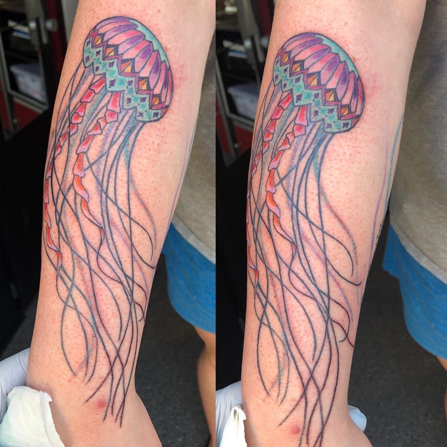 Colorful jellyfish tattoo on person's forearm with pink, purple, green, and orange hues, and flowing tentacles.