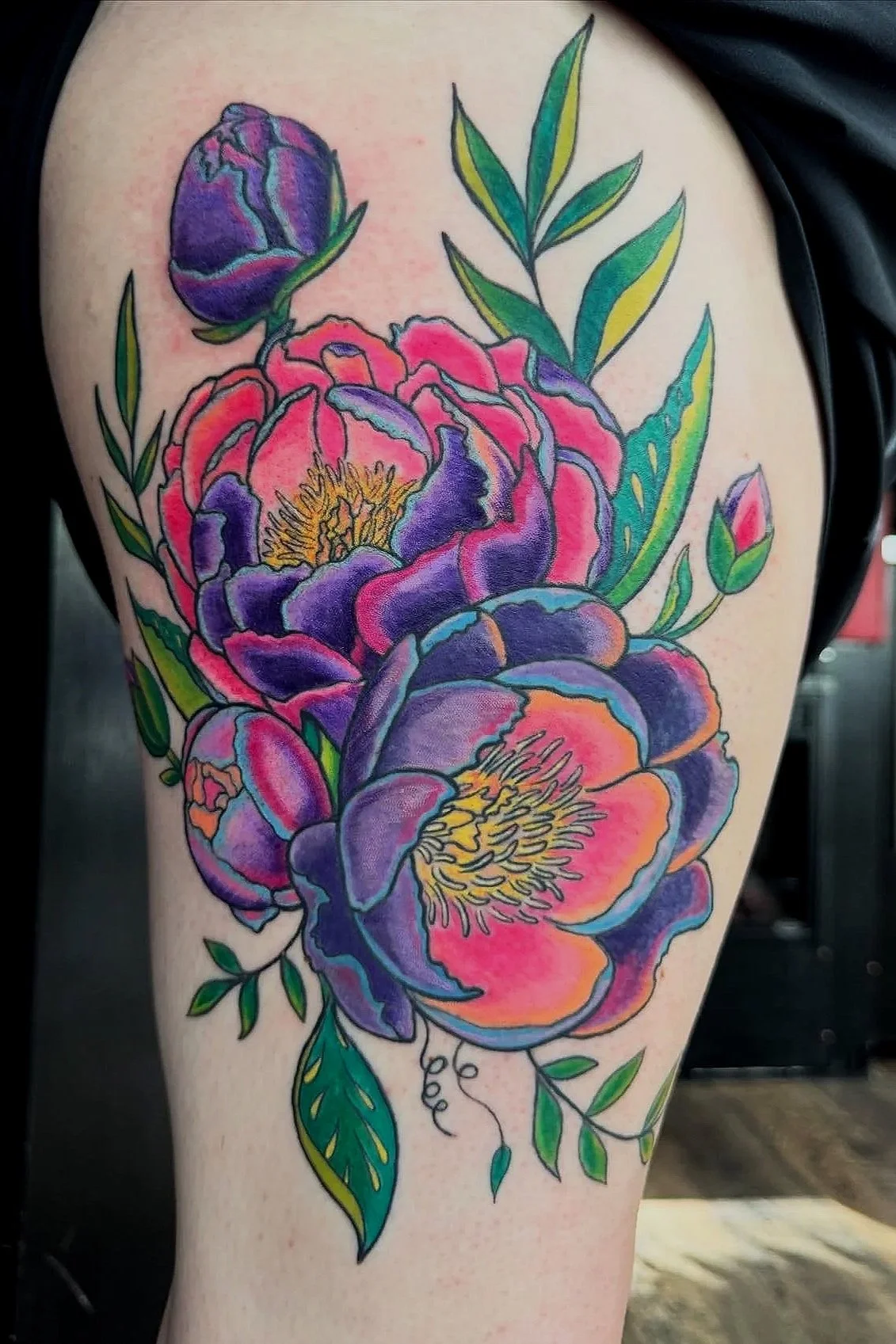 Colorful floral tattoo featuring large peony flowers in shades of purple, pink, and orange, with green leaves and stems.