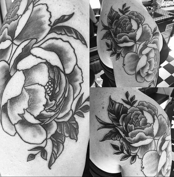 Black and white tattoo of a large peony flower with leaves, shown on a person's shoulder and upper arm.