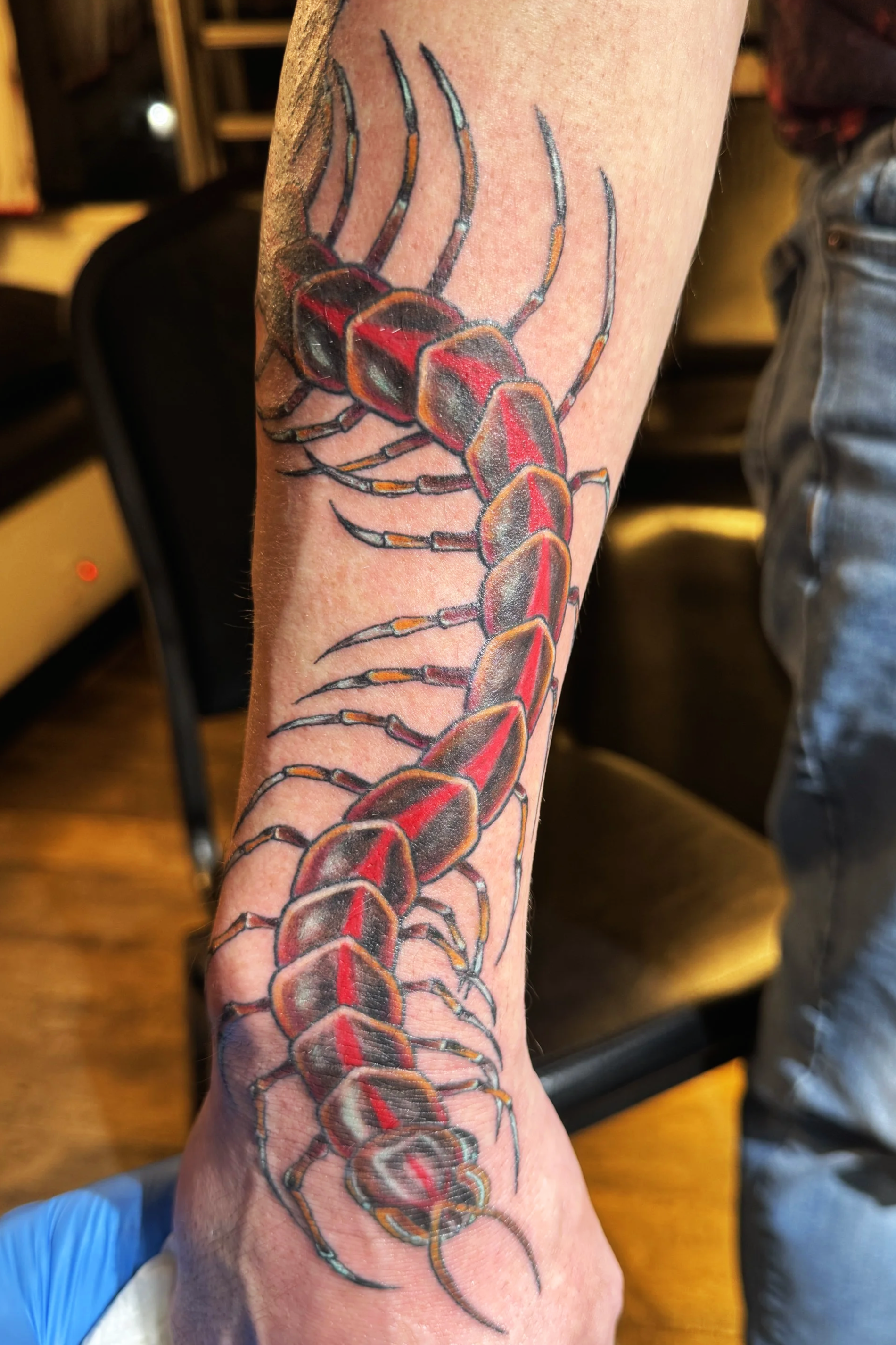 A detailed tattoo of a centipede on a person's lower arm.