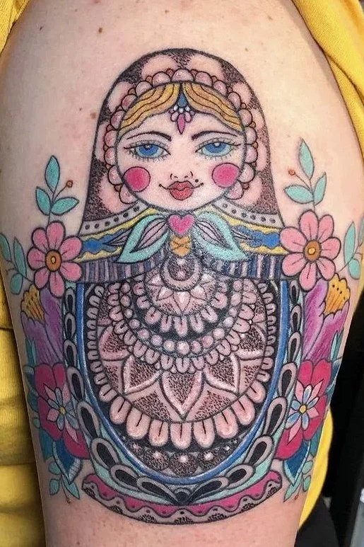 Colorful tattoo of a stylized face with blue eyes, pink cheeks, and red lips, surrounded by flowers and decorative patterns.