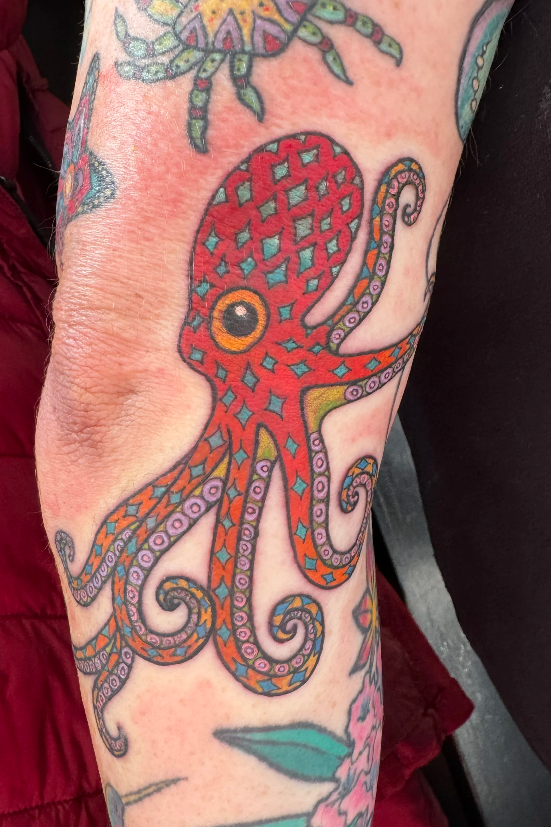 Colorful tattoo of a stylized octopus with intricate patterns on its body and tentacles, located on a person's arm.