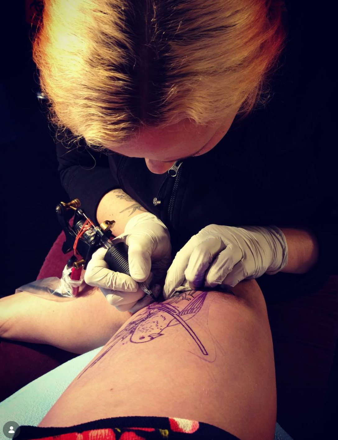 Tattoo artist creating a bird tattoo on a person's thigh with a tattoo machine.