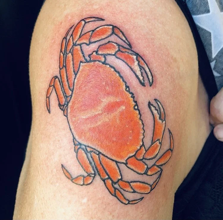 A colorful tattoo of a crab on someone's skin, with orange and red hues and black outlines.