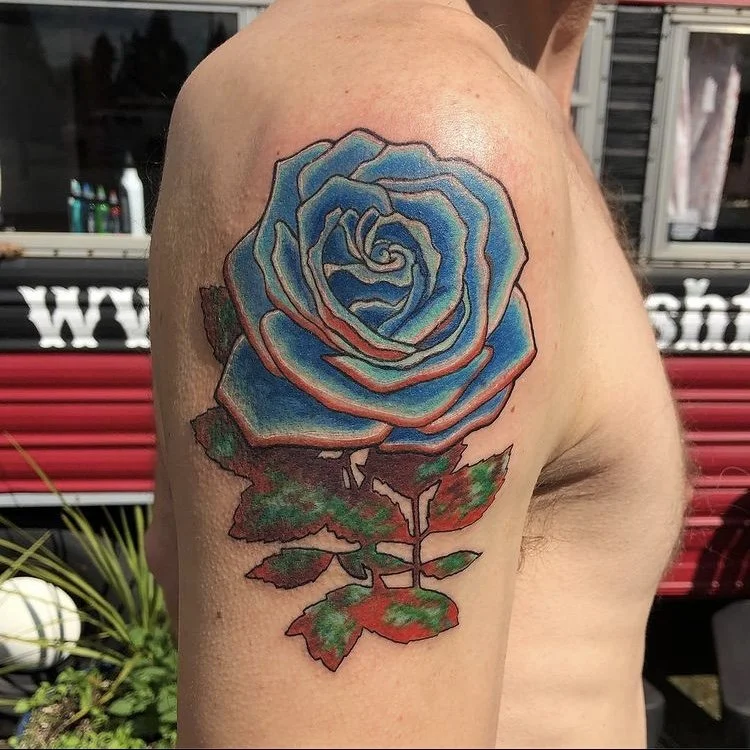 Tattoo of a blue and pink rose with green and red leaves on a person's upper arm.