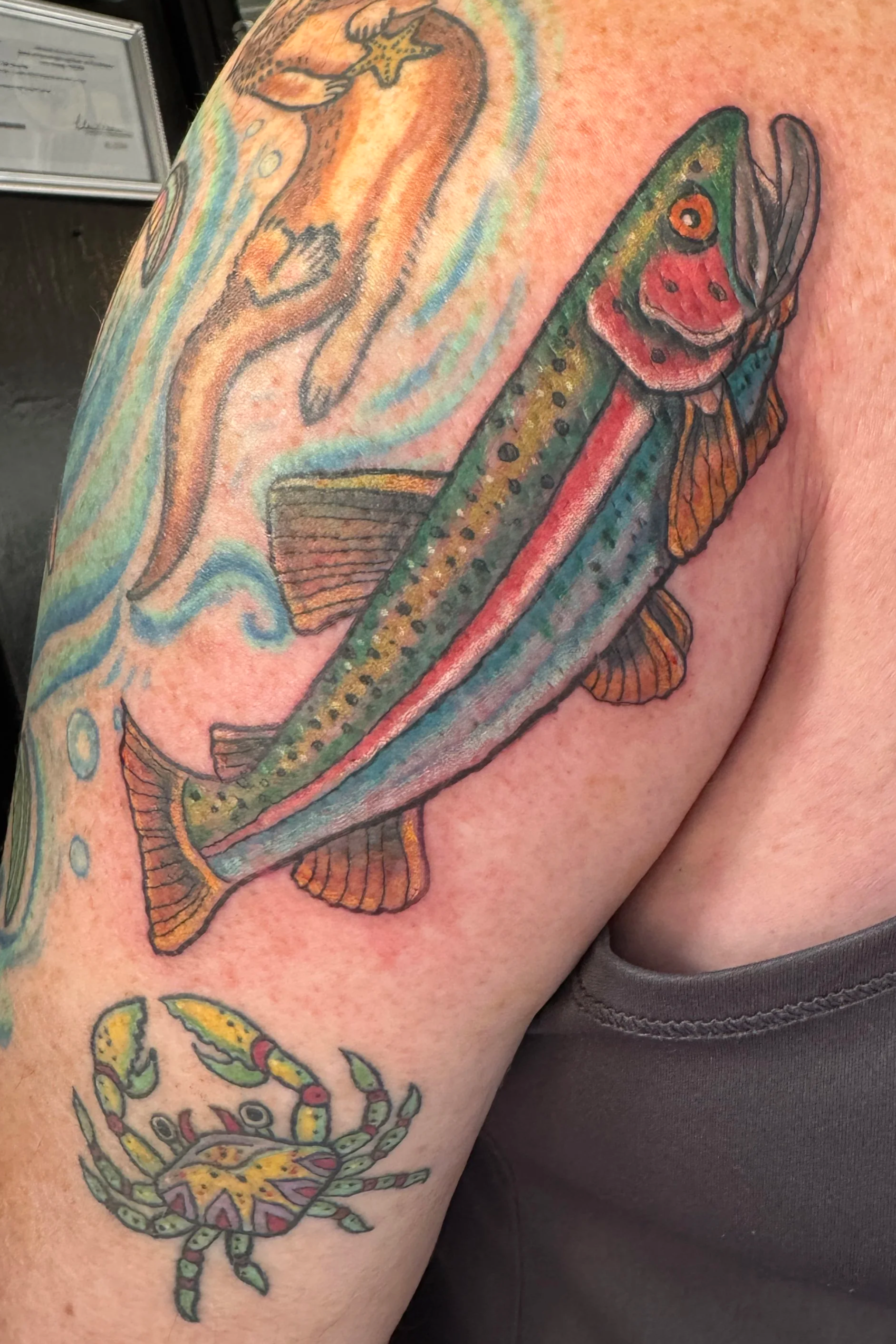 Tattoo of a colorful fish and a crab on a person's arm.