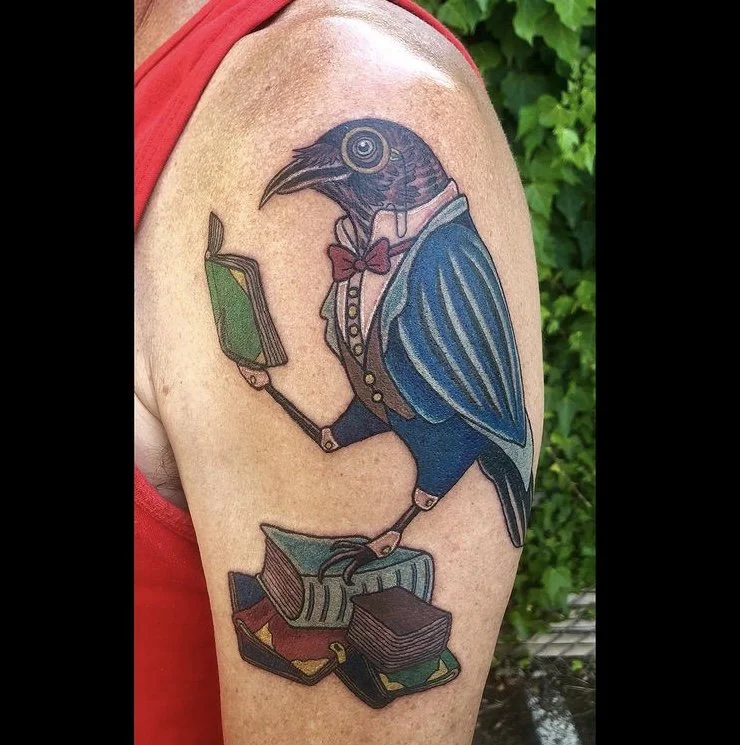 Tattoo of a bird with a human body, wearing a suit, reading a book while sitting on stacked books.