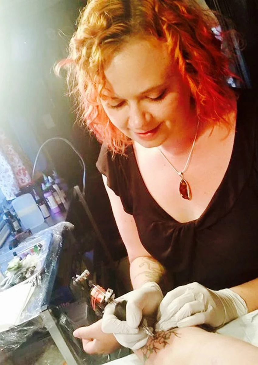 A woman with curly red hair getting a tattoo on her arm.