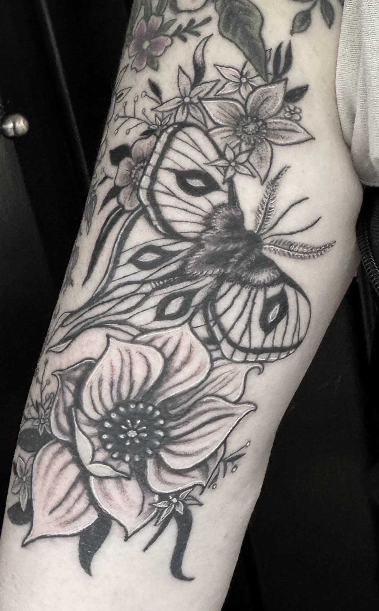 Black and gray tattoo on person's upper arm featuring flowers and a bee.
