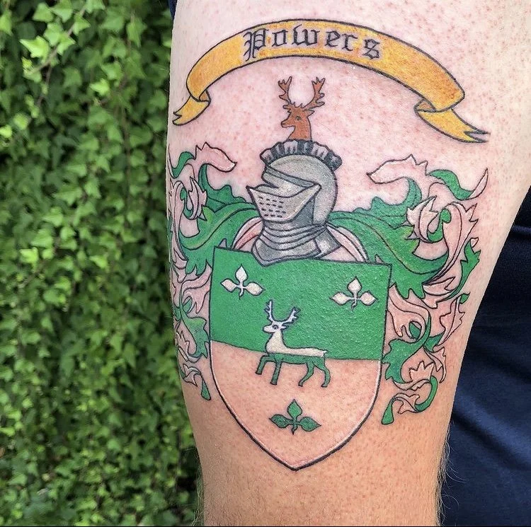 A colorful tattoo of a shield with a deer on top and a banner with the word "Futures" above. The shield contains a stylized reindeer and decorative elements, with green, pink, and gray colors, alongside a decorative crest with a deer helmet and flora