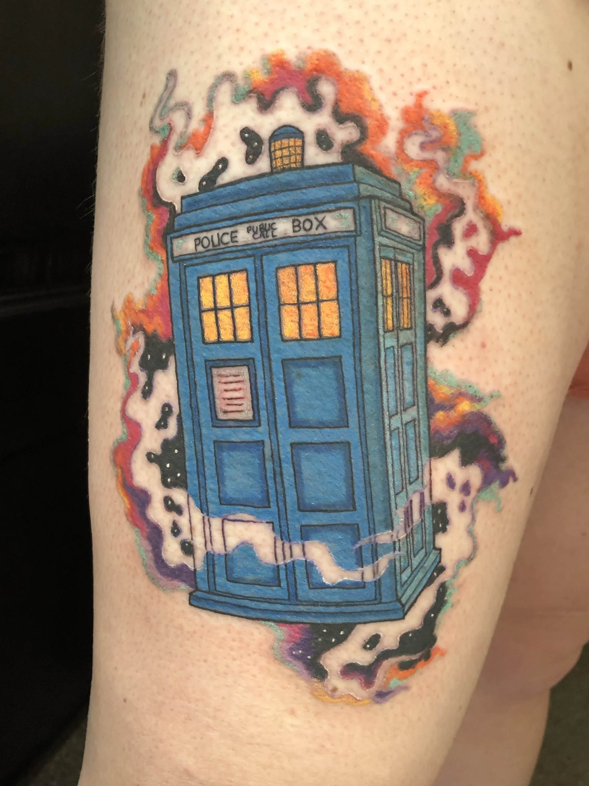 Colorful tattoo of the TARDIS from Doctor Who on person's arm, emitting colorful smoke.