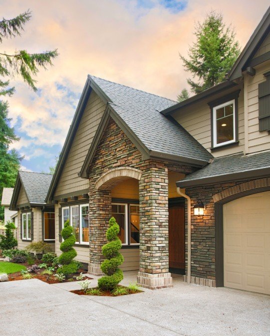 Exterior view of a modern suburban house with a brick and siding facade, a gabled roof, and manicured landscaping including spiral-shaped topiary bushes.