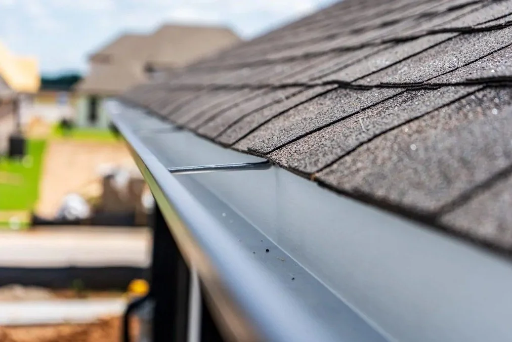 Close-up of a house roof with asphalt shingles and a metal gutter.