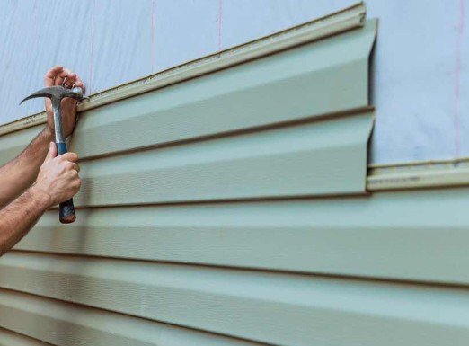 Person using a hammer to install or repair horizontal siding or paneling on a building.