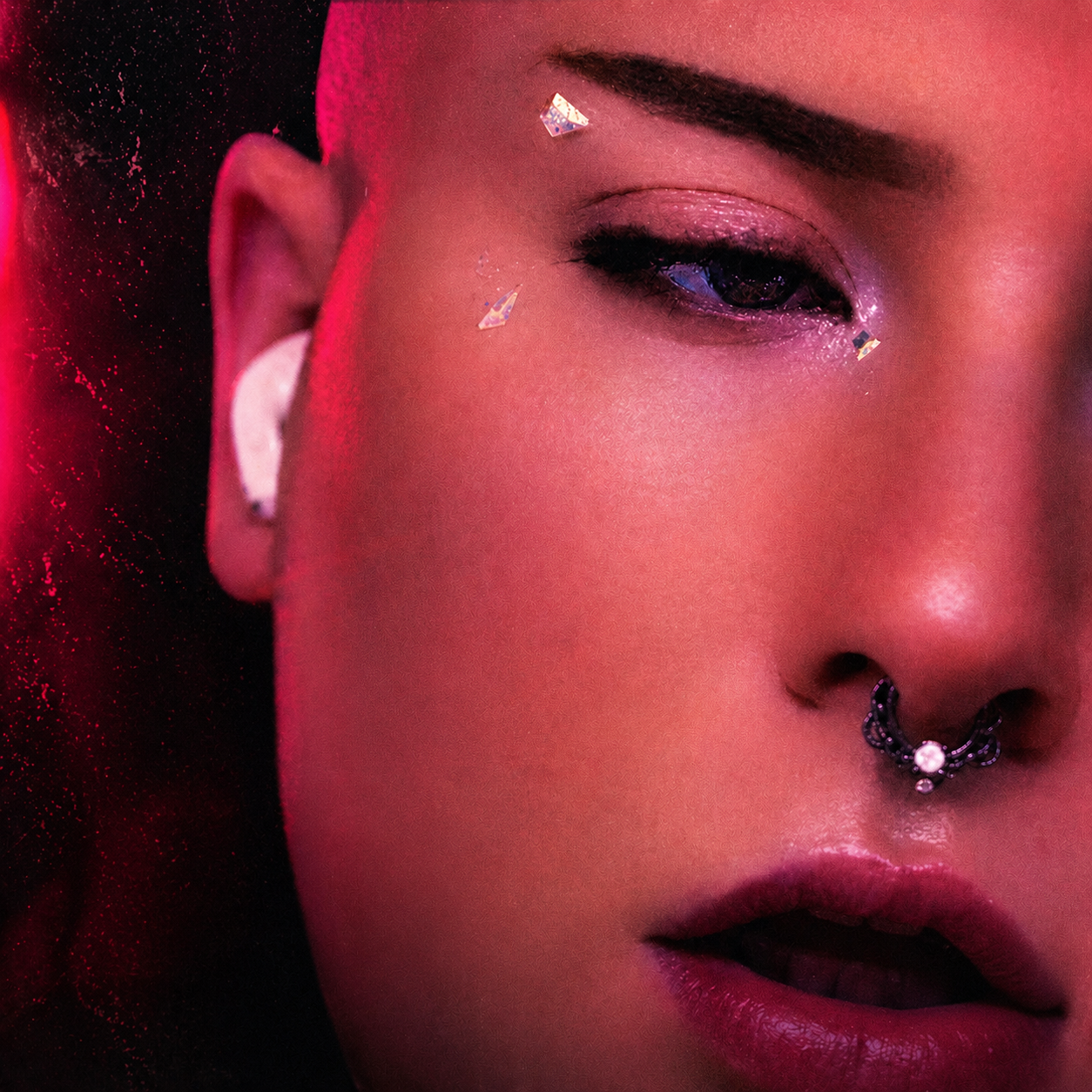 Close-up of a person's face with makeup, jewelry, and face gems, with a dark background.