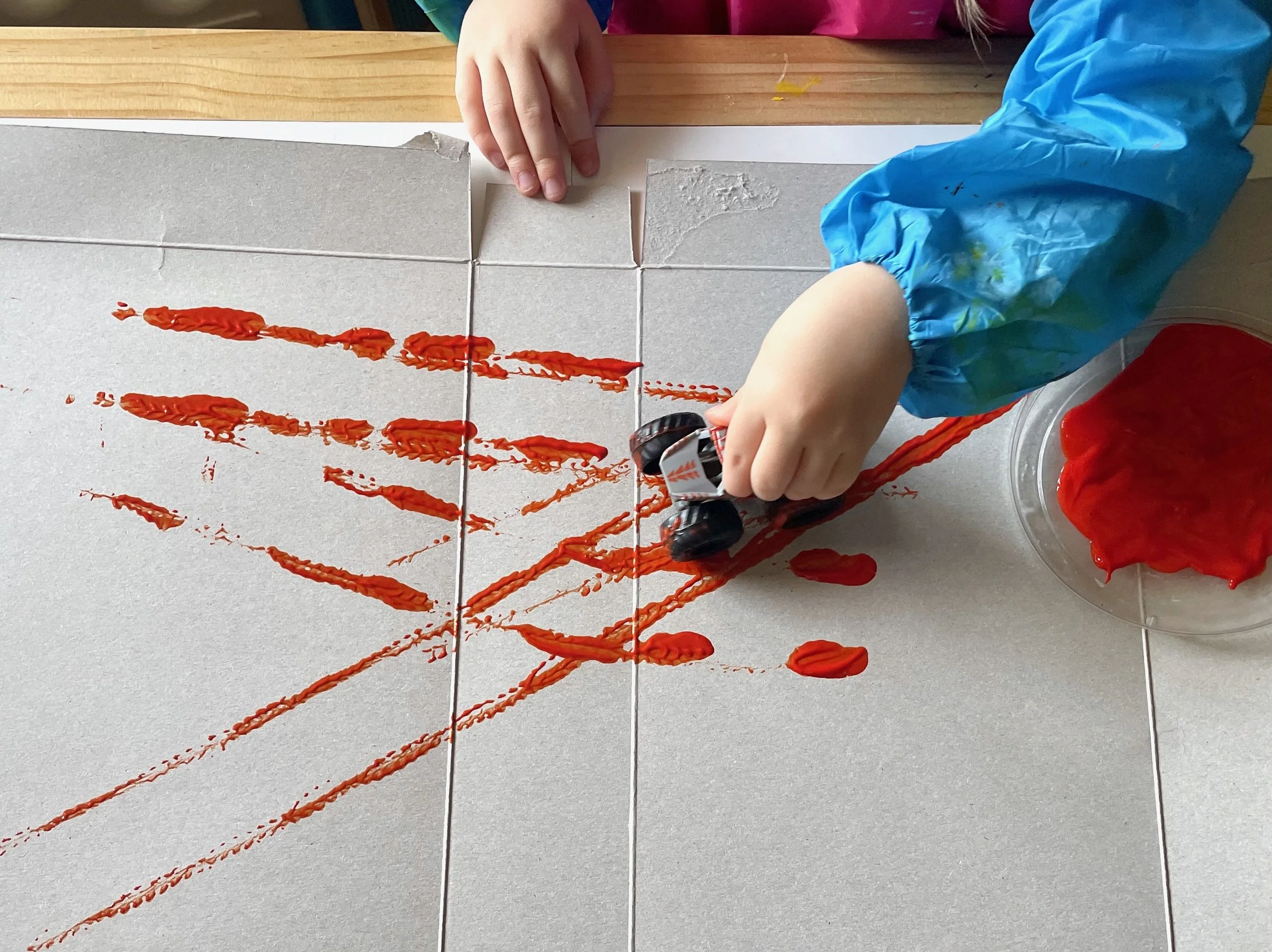 Child painting with red paint on a tiled surface, using a small roller, with a blue sleeve visible on their arm.