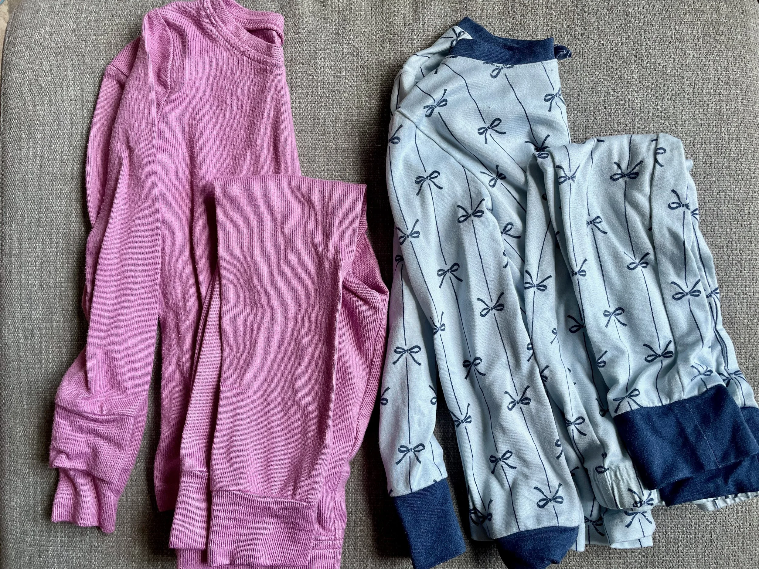 Pink long sleeve shirt and a pair of light gray and navy blue pajama pants with bow patterns laid out on a beige fabric surface.