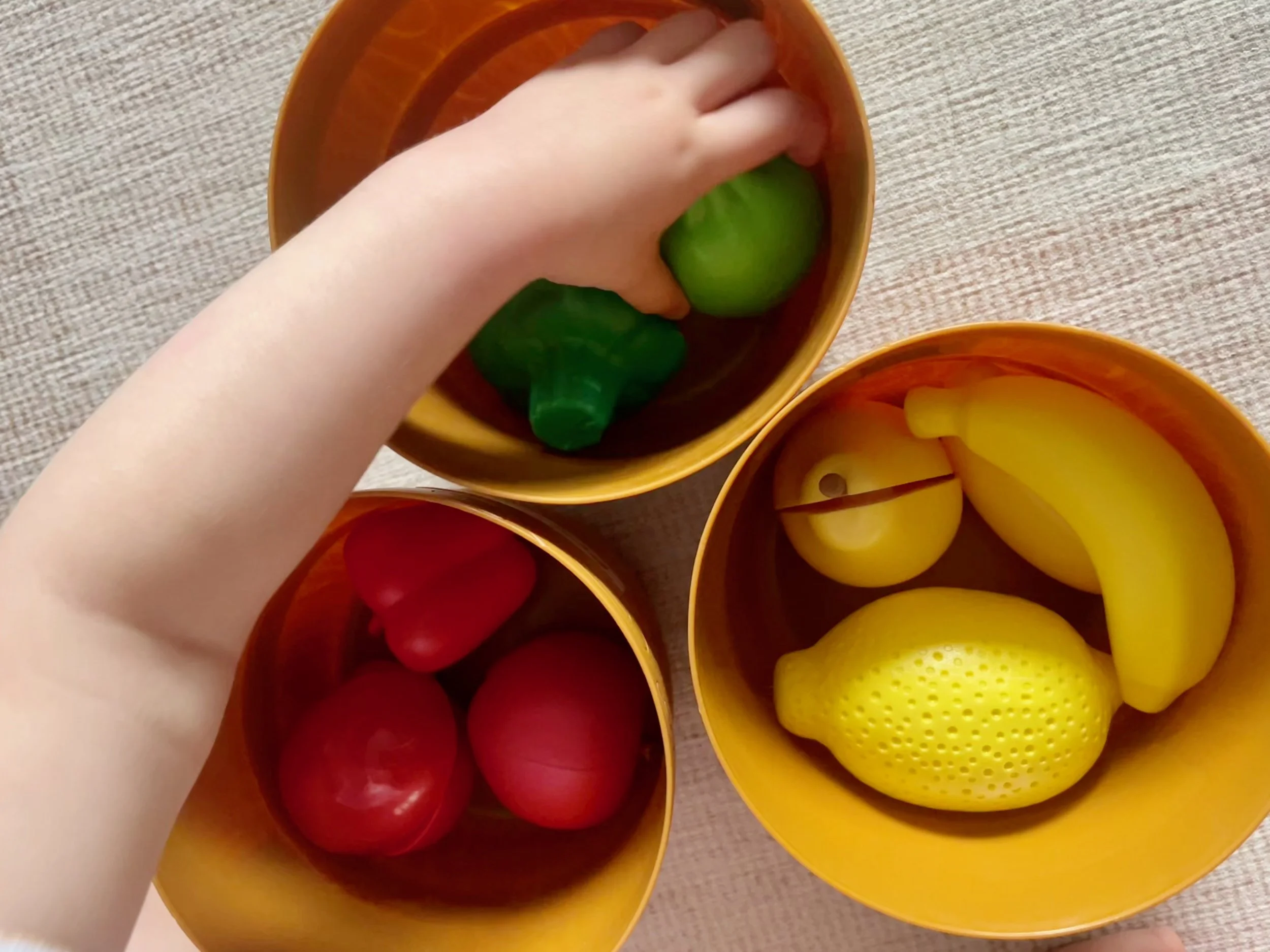 Colored plastic balls in yellow, orange, and red containers. A child's hand reaching into the green ball container.